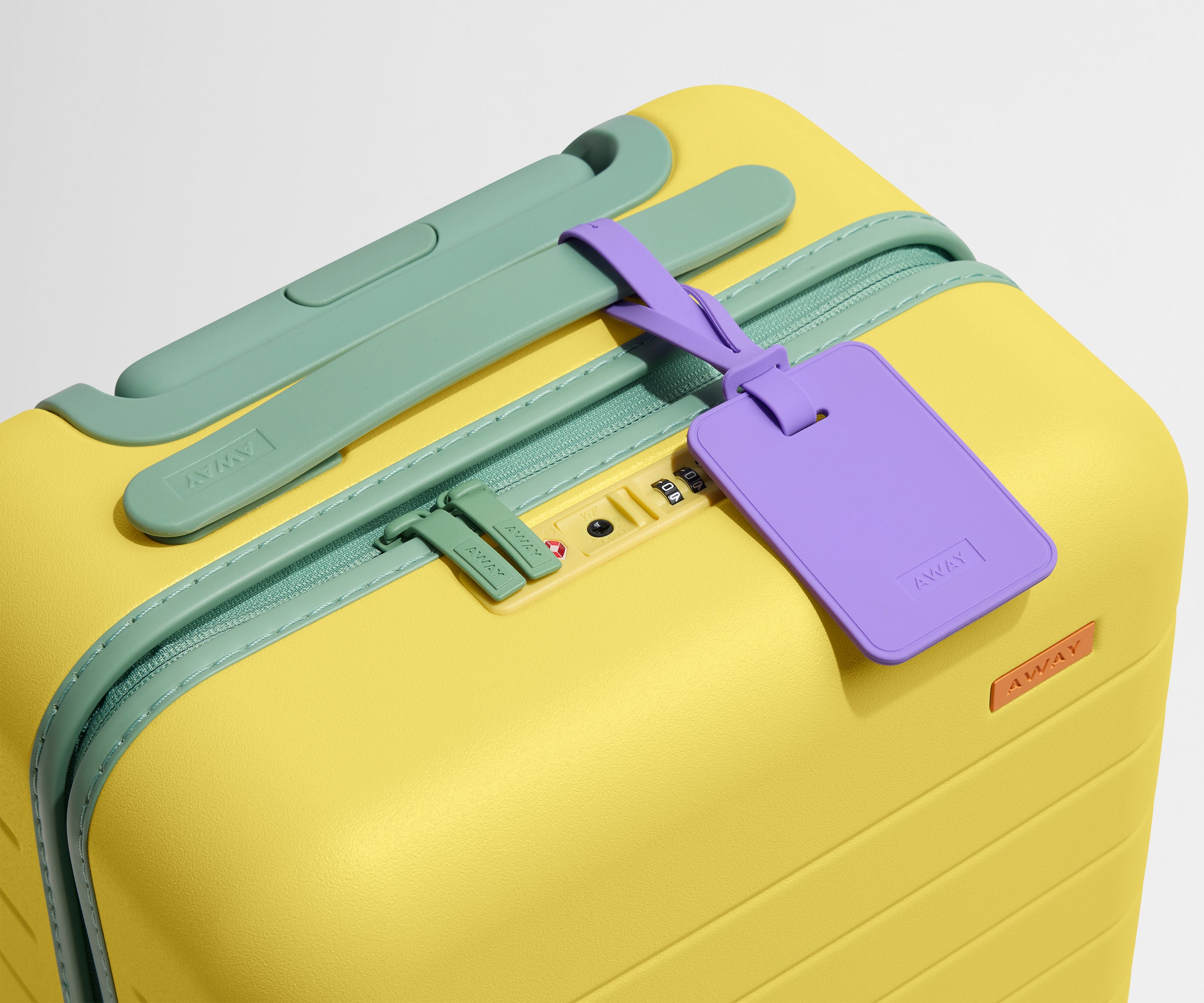 The Kids Carry-On suitcase in Sunshine Yellow shown shown from above highlighting TSA-approved combination lock and colorful silicone luggage tag