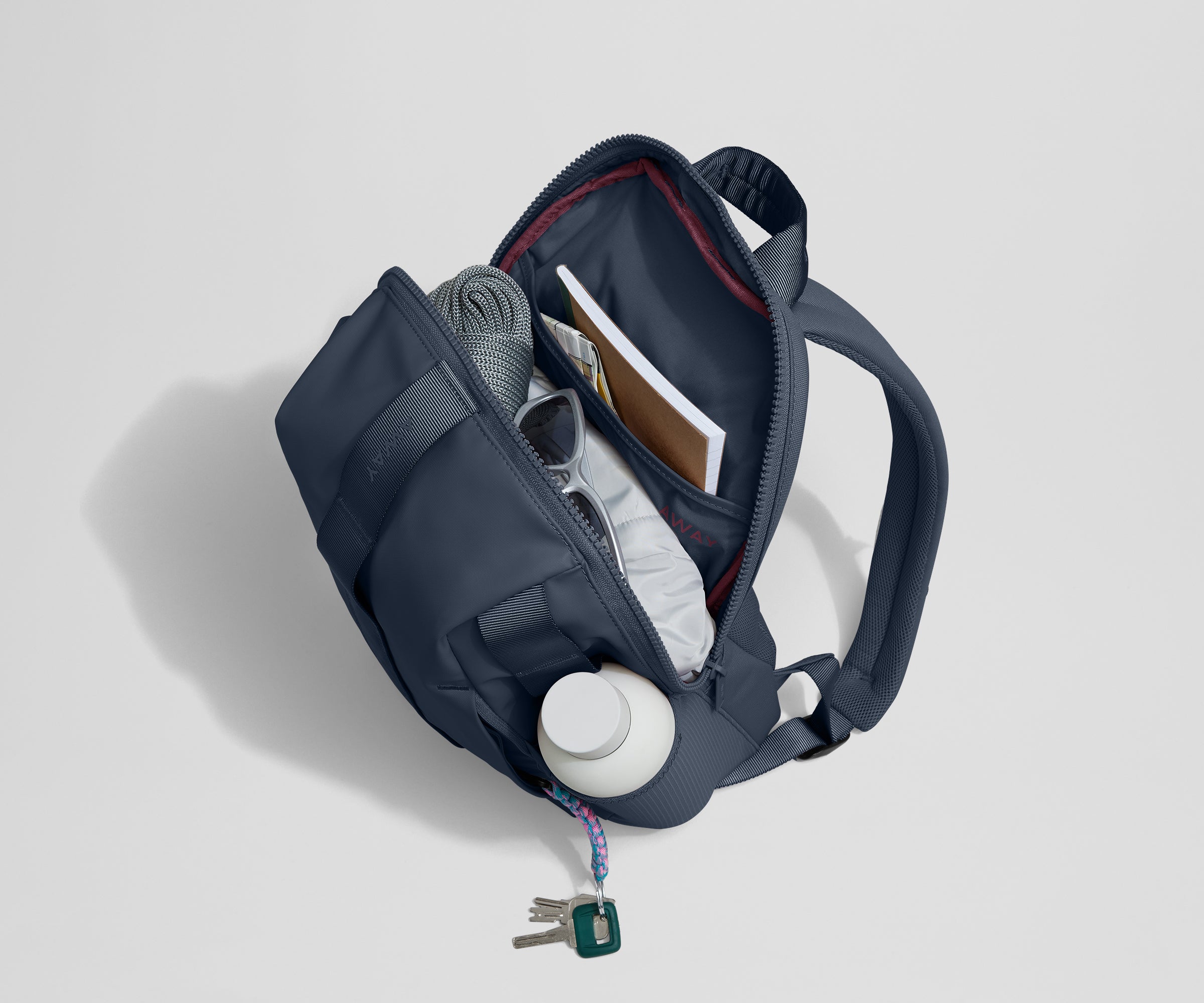 Daypack packed with a light jacket, sunglasses, notebook, map, and other travel gear. Water bottle featured in the exterior water bottle pocket.