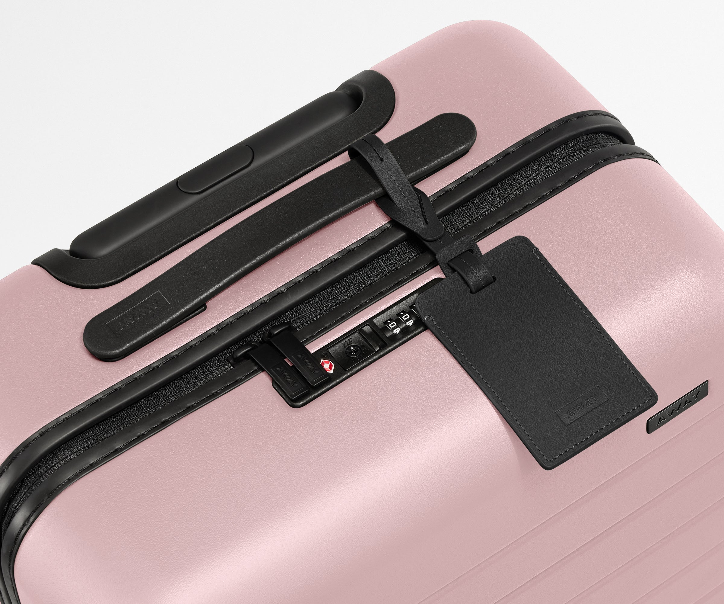 The Bigger Carry-On suitcase in Blush Pink shown shown from above highlighting TSA-approved combination lock and recycled leather luggage tag