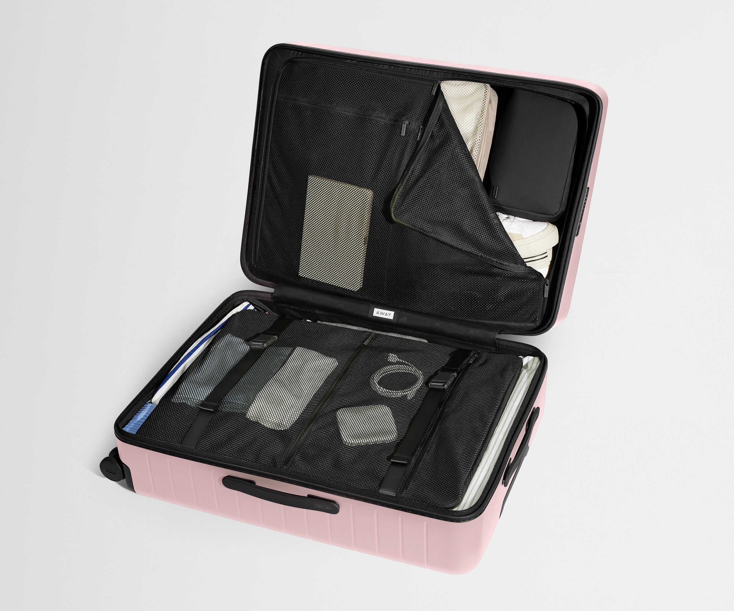 The Large suitcase in Blush Pink shown open on its side and packed with Away's packing organizers to show capacity and the interior compression system, designed to help you pack more in