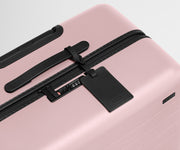 The Large suitcase in Blush Pink shown shown from above highlighting TSA-approved combination lock and recycled leather luggage tag
