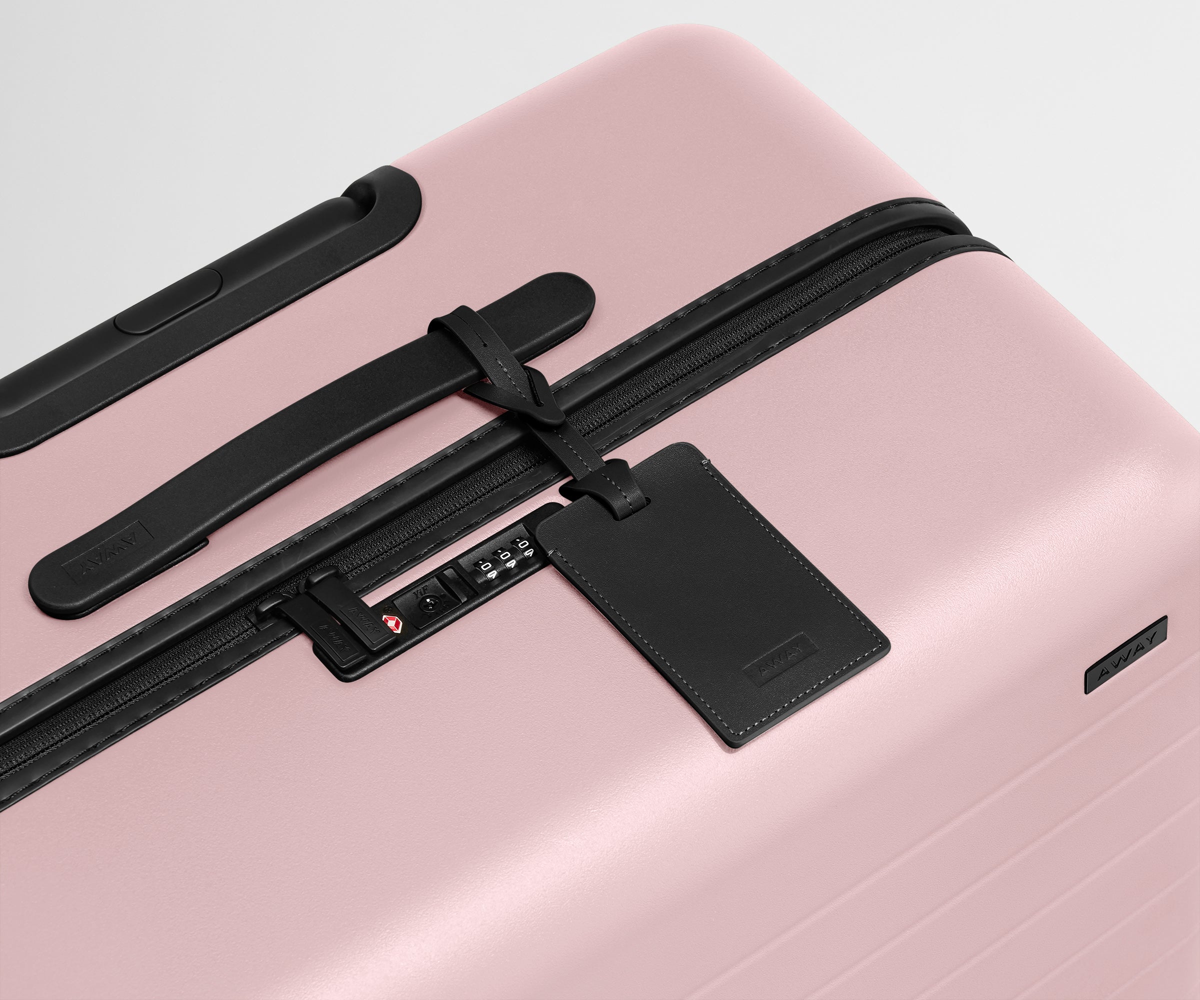 The Large suitcase in Blush Pink shown shown from above highlighting TSA-approved combination lock and recycled leather luggage tag