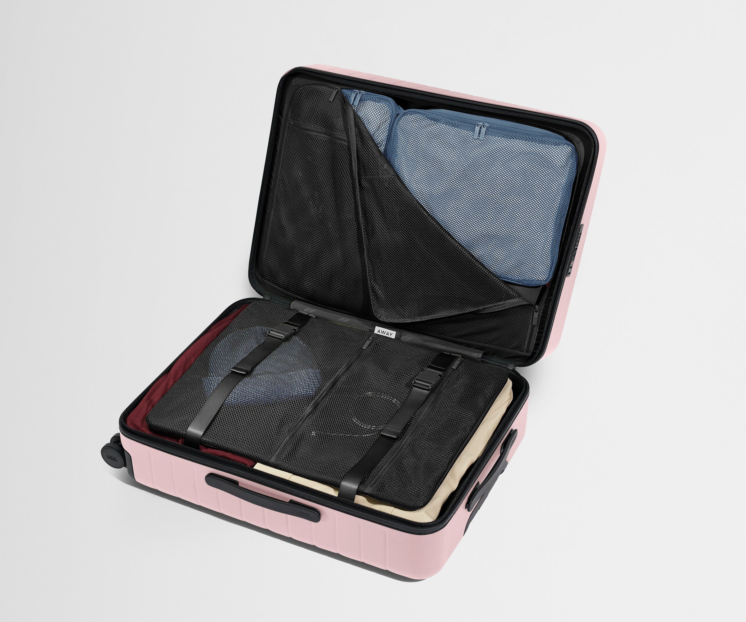 The Medium suitcase in Blush Pink shown open on its side and packed with Away's packing organizers to show capacity and the interior compression system, designed to help you pack more in