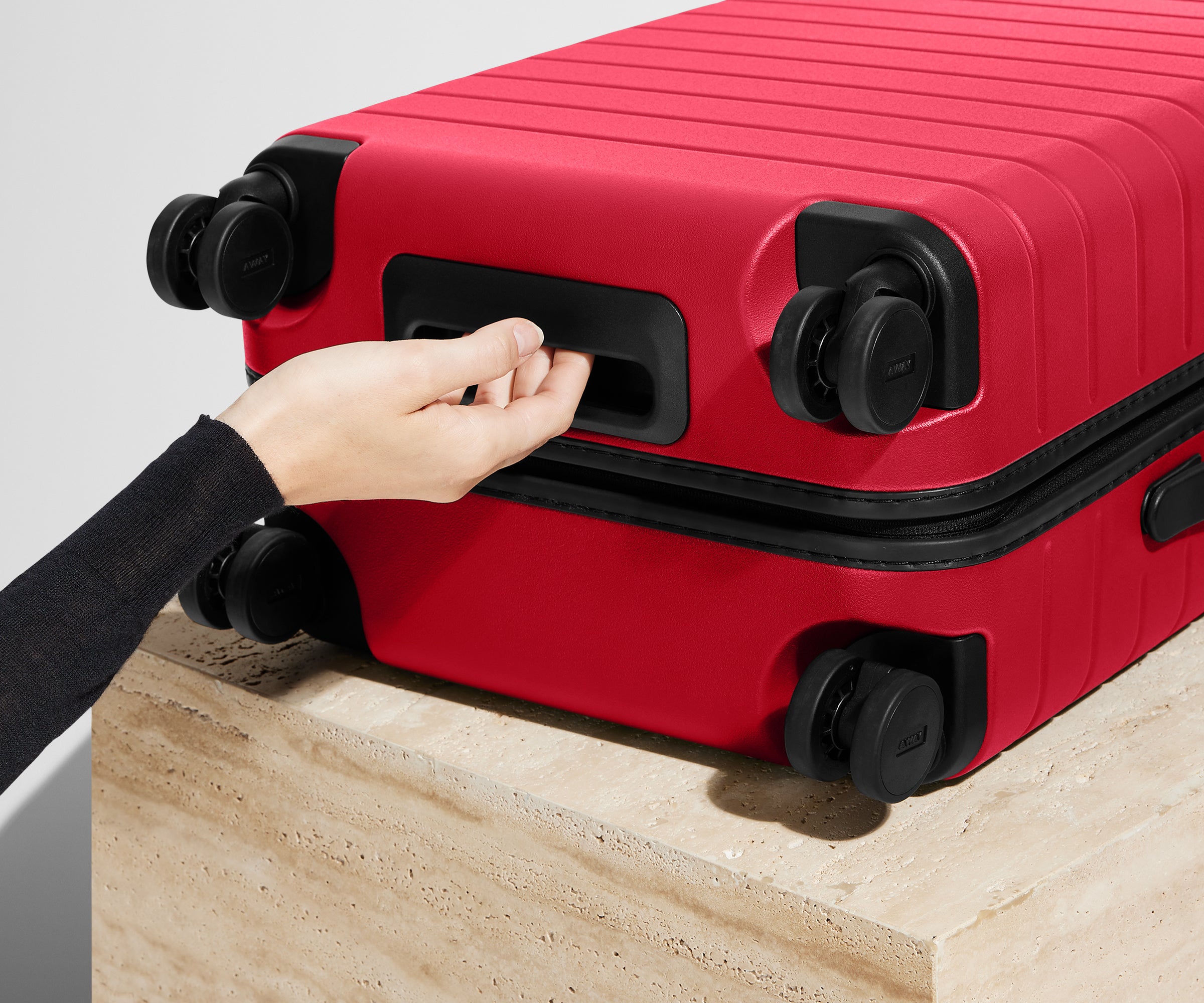 Red suitcase with a hand reaching to open it on a light wooden surface.