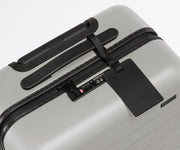 The Carry-On suitcase in Cloud Gray shown shown from above highlighting TSA-approved combination lock and recycled leather luggage tag