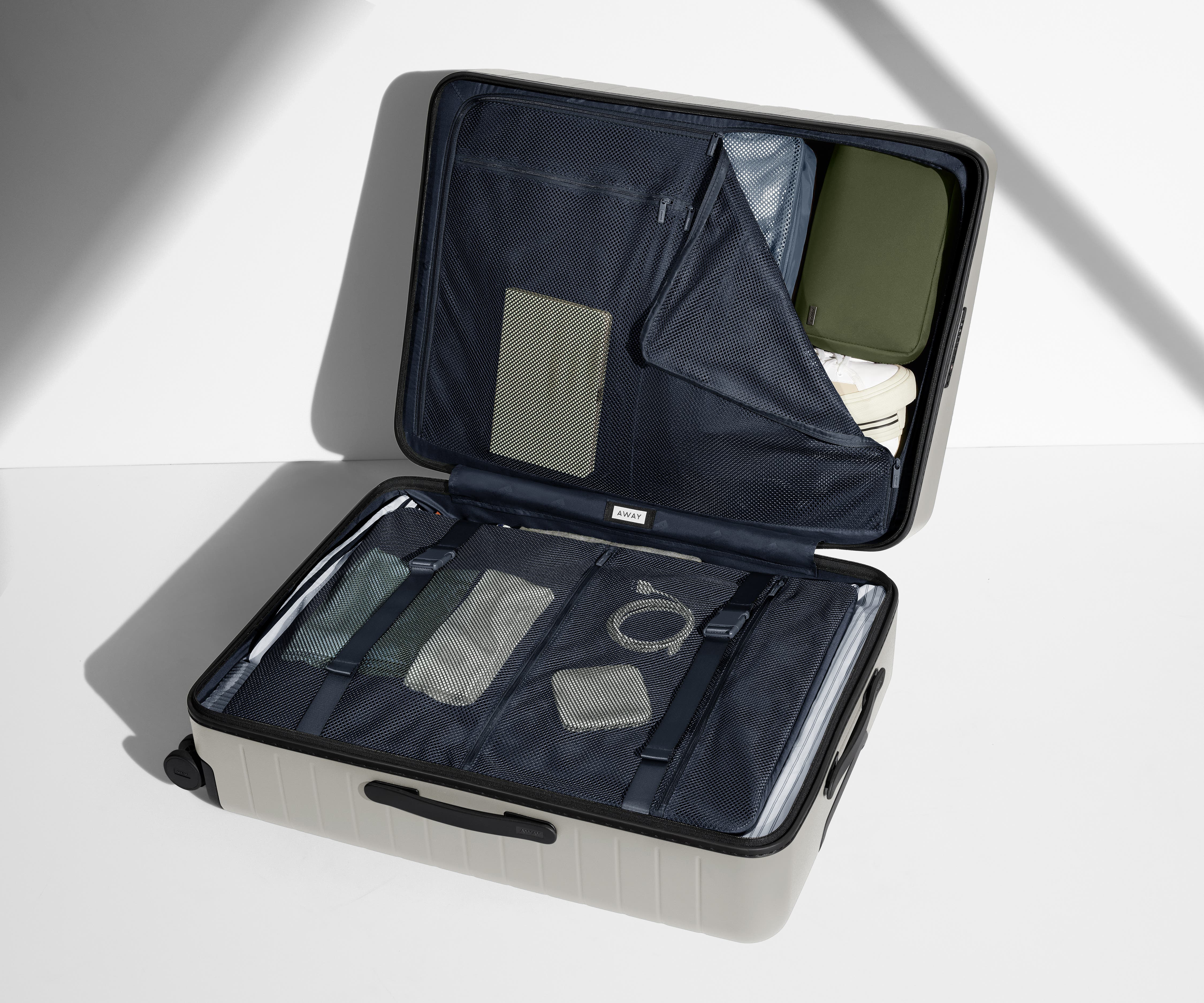 The Large suitcase in Cloud Gray shown open on its side and packed with Away's packing organizers to show capacity and the interior compression system, designed to help you pack more in