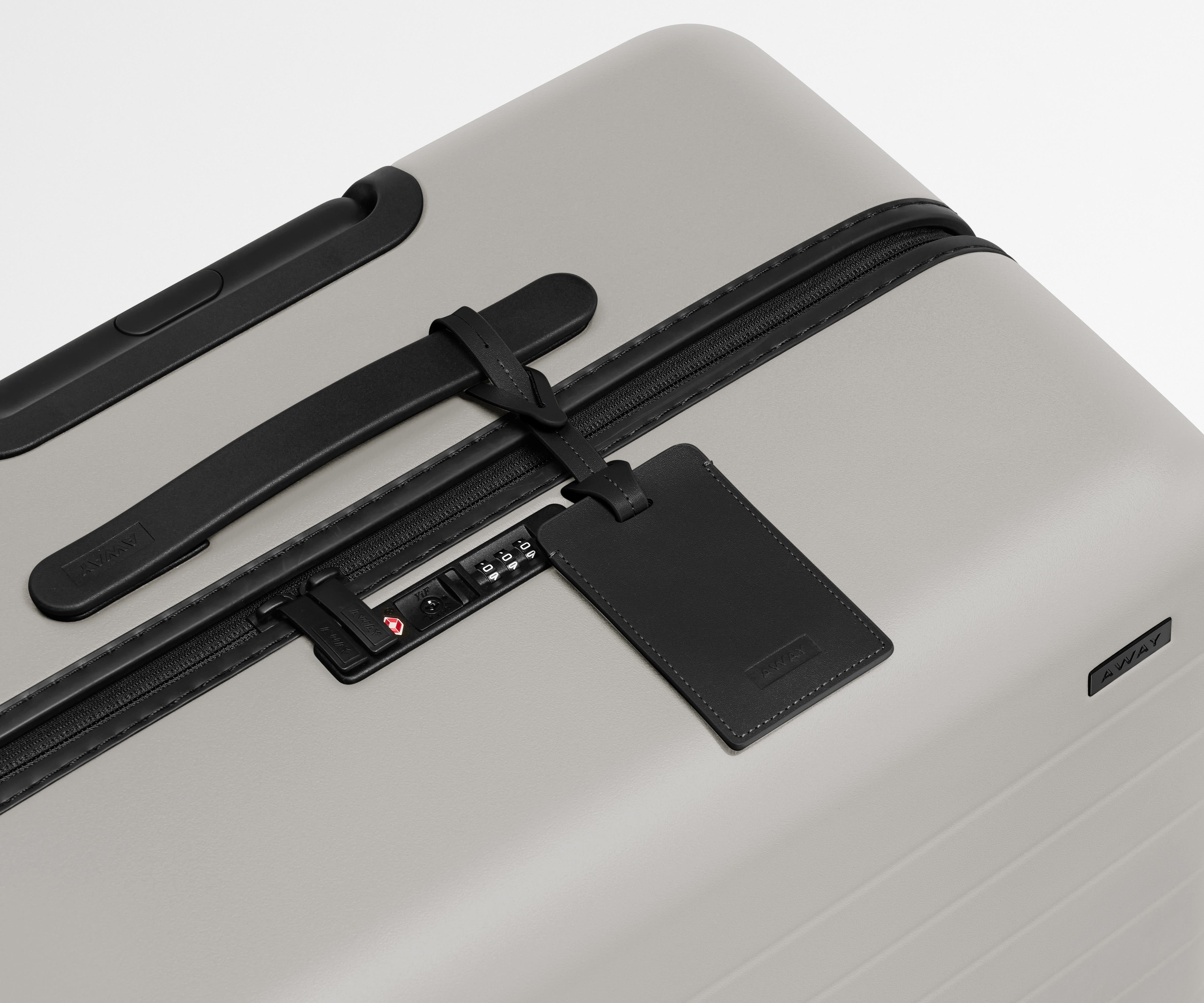 The Medium suitcase in Cloud Gray shown shown from above highlighting TSA-approved combination lock and recycled leather luggage tag