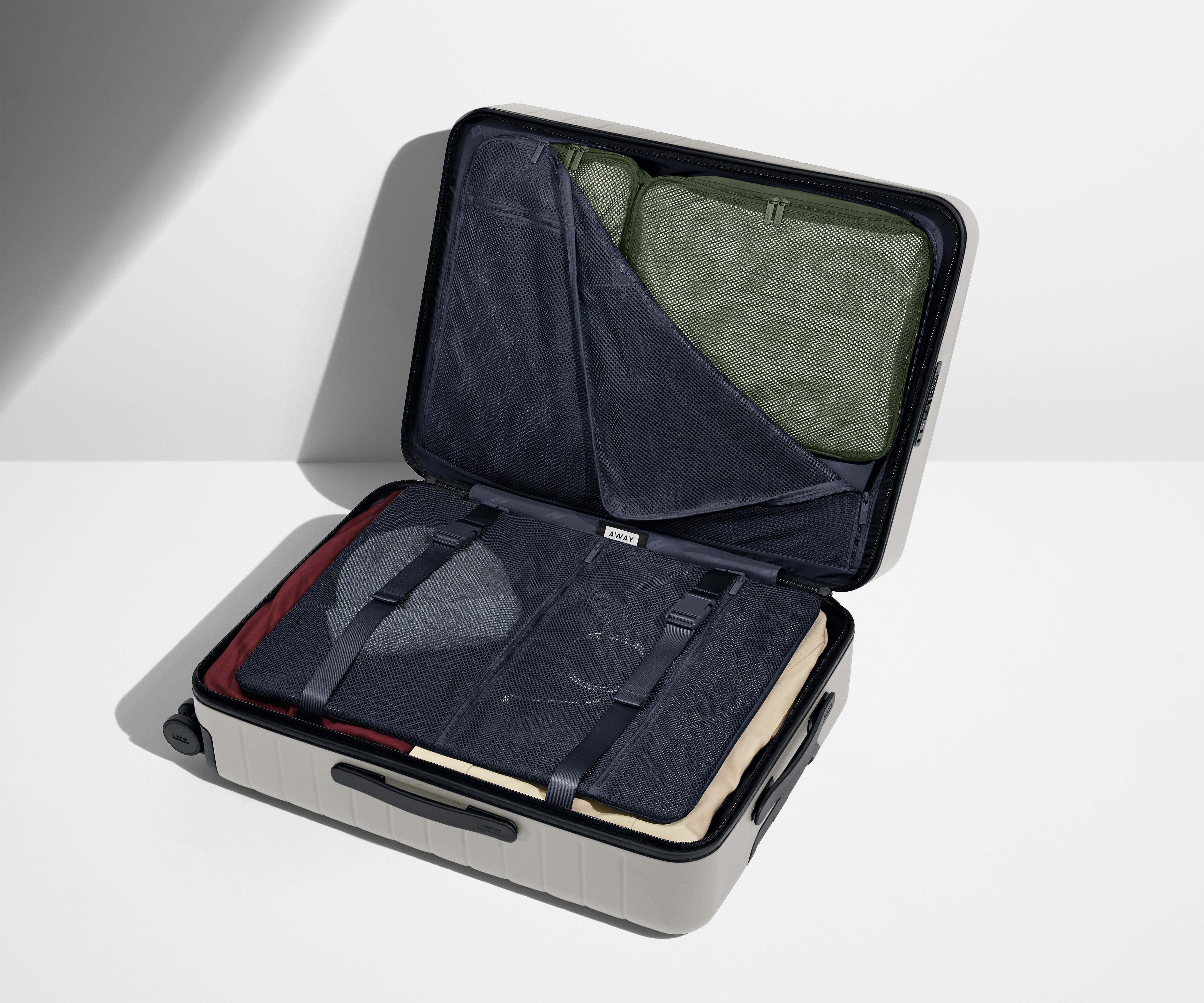 The Medium suitcase in Cloud Gray shown open on its side and packed with Away's packing organizers to show capacity and the interior compression system, designed to help you pack more in