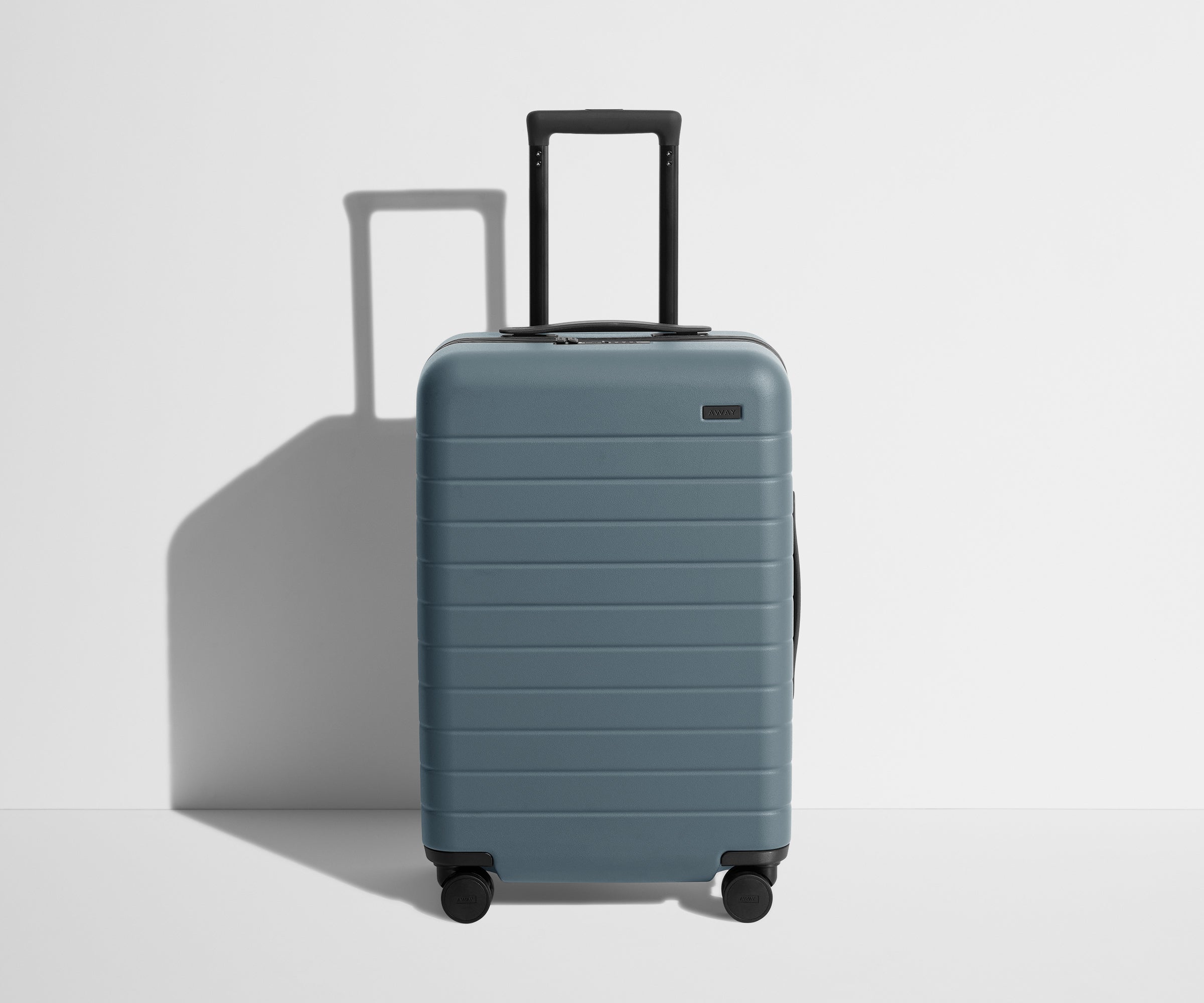 Front product view of The Bigger Carry-On suitcase in Coast Blue with raised handle