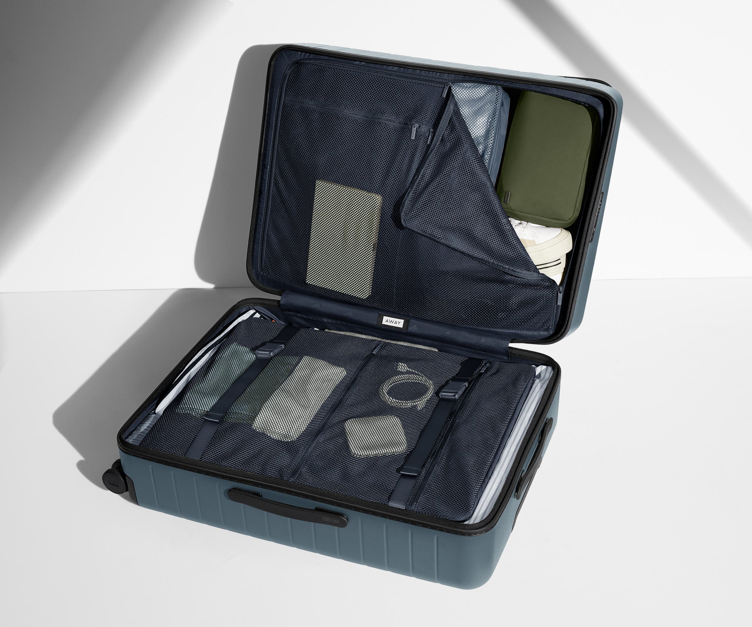 The Large suitcase in Coast Blue shown open on its side and packed with Away's packing organizers to show capacity and the interior compression system, designed to help you pack more in
