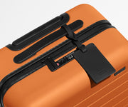 The Carry-On suitcase in Sorbet Orange shown shown from above highlighting TSA-approved combination lock and recycled leather luggage tag