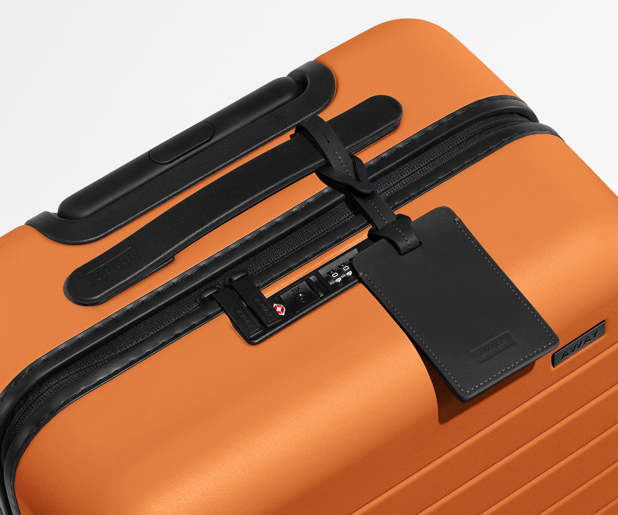 The Carry-On suitcase in Sorbet Orange shown shown from above highlighting TSA-approved combination lock and recycled leather luggage tag
