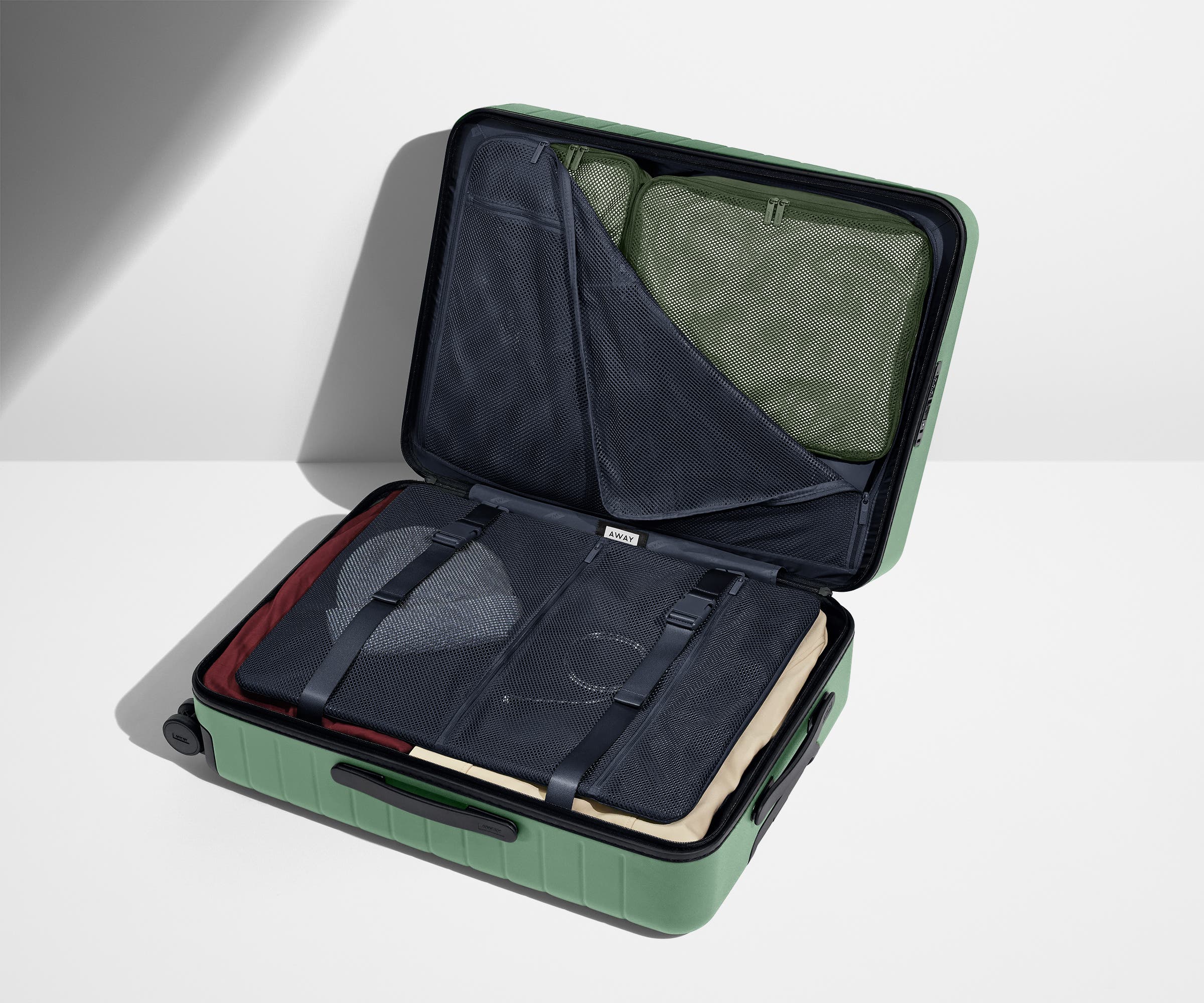 The Medium suitcase in Sea Green shown open on its side and packed with Away's packing organizers to show capacity and the interior compression system, designed to help you pack more in