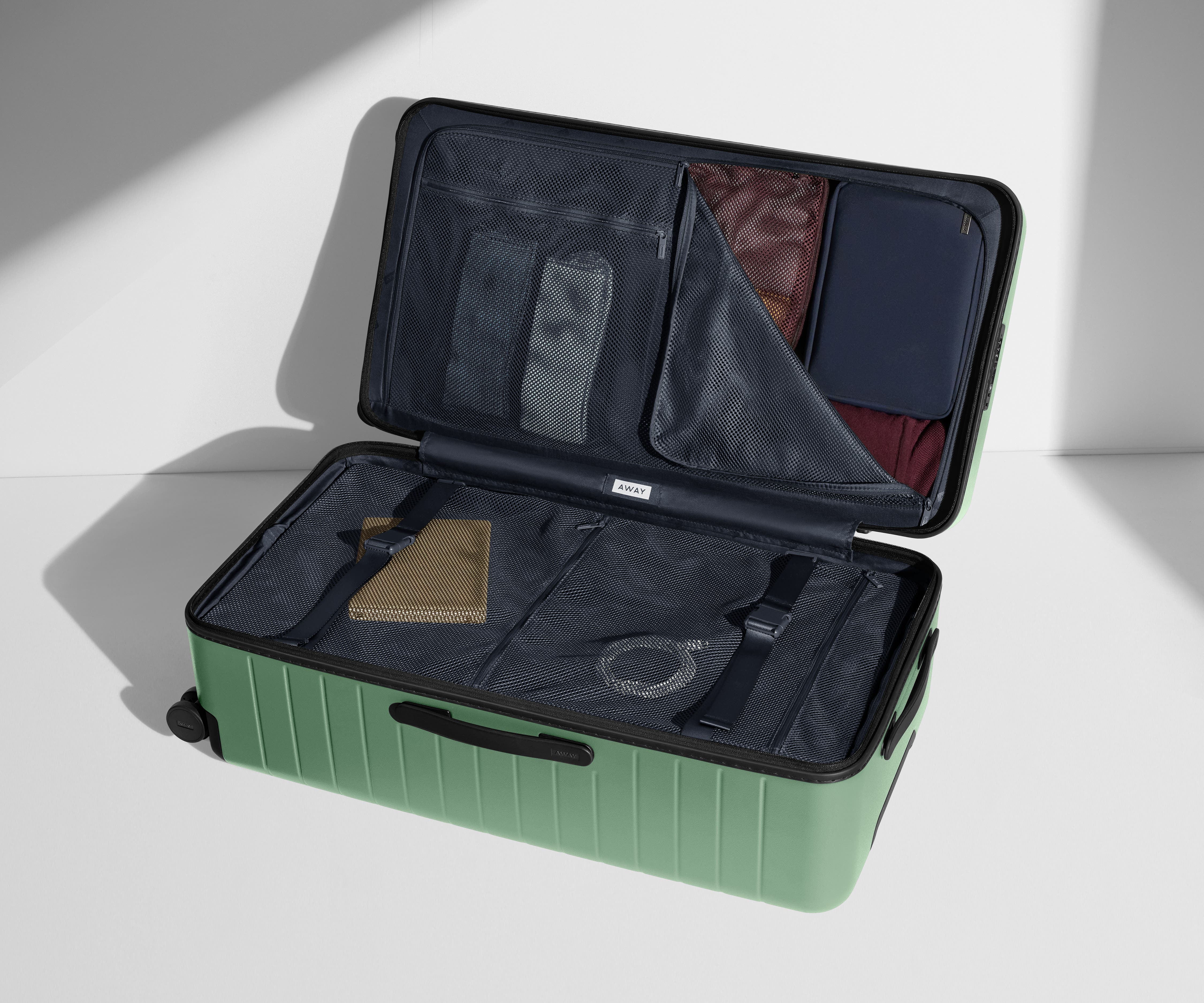 The Trunk suitcase in Sea Green shown open on its side and packed with Away's packing organizers to show capacity and the interior compression system, designed to help you pack more in