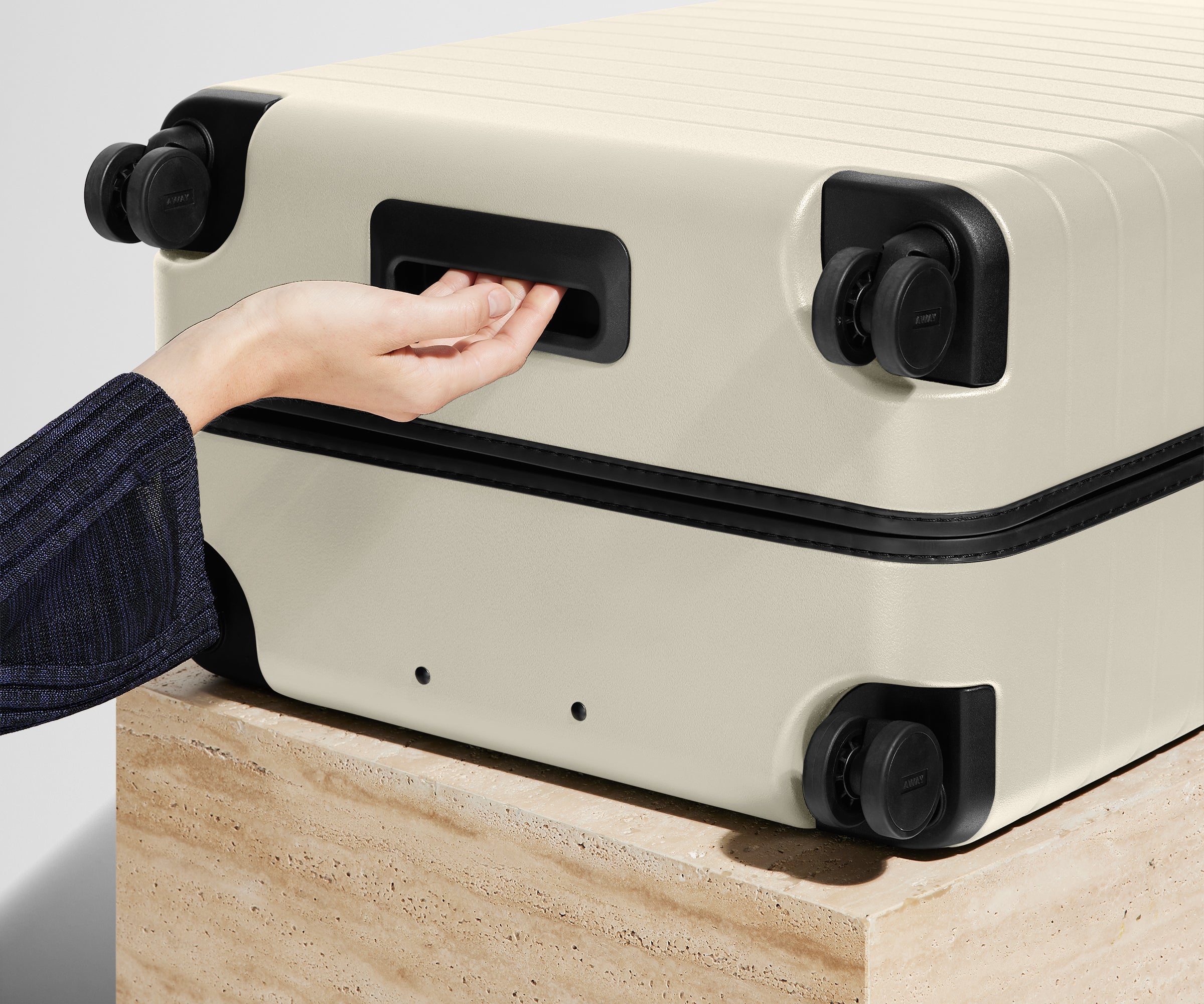 White suitcase with black handles and wheels on a light wooden surface.