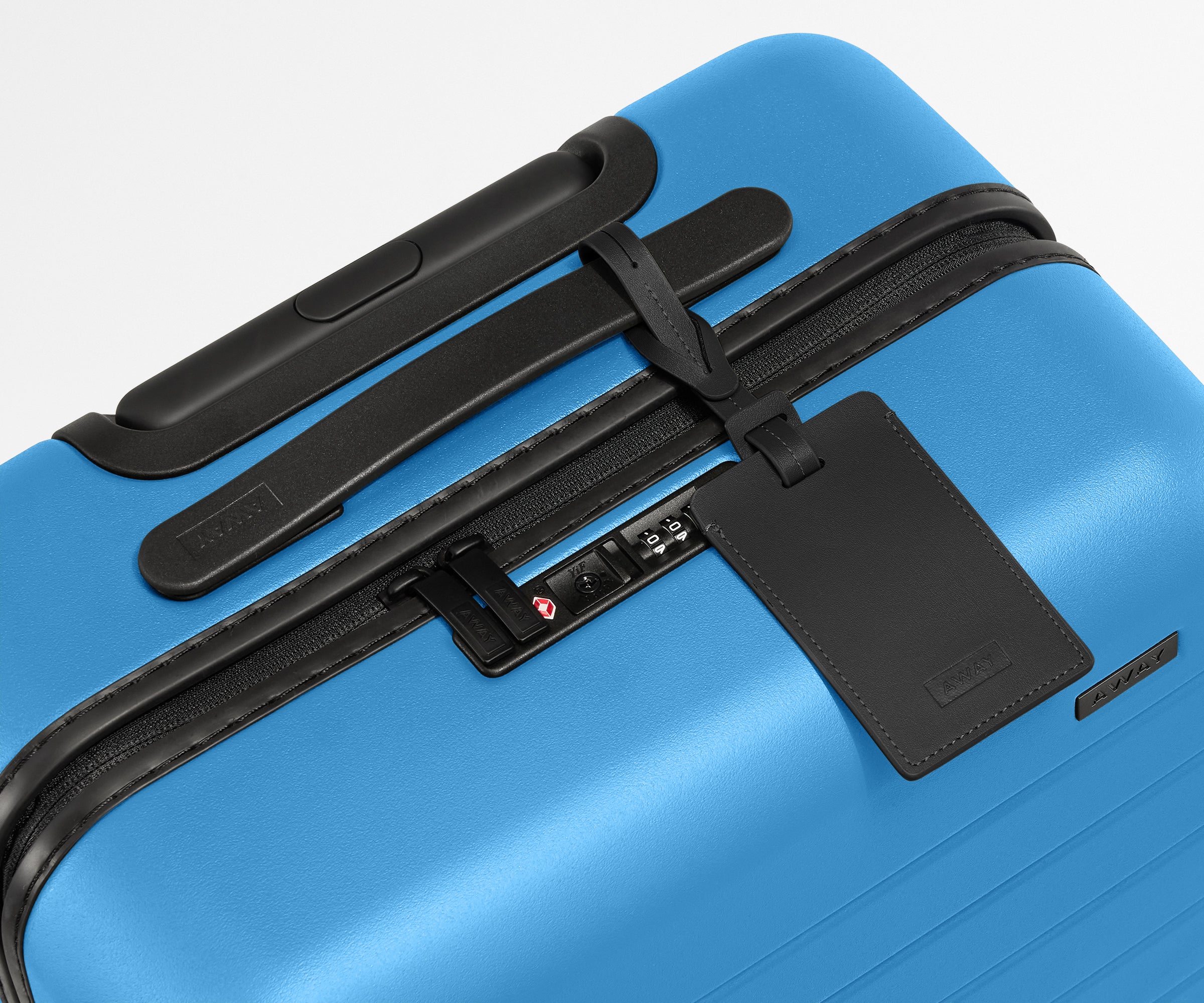 The Bigger Carry-On suitcase in Splash Blue shown shown from above highlighting TSA-approved combination lock and recycled leather luggage tag