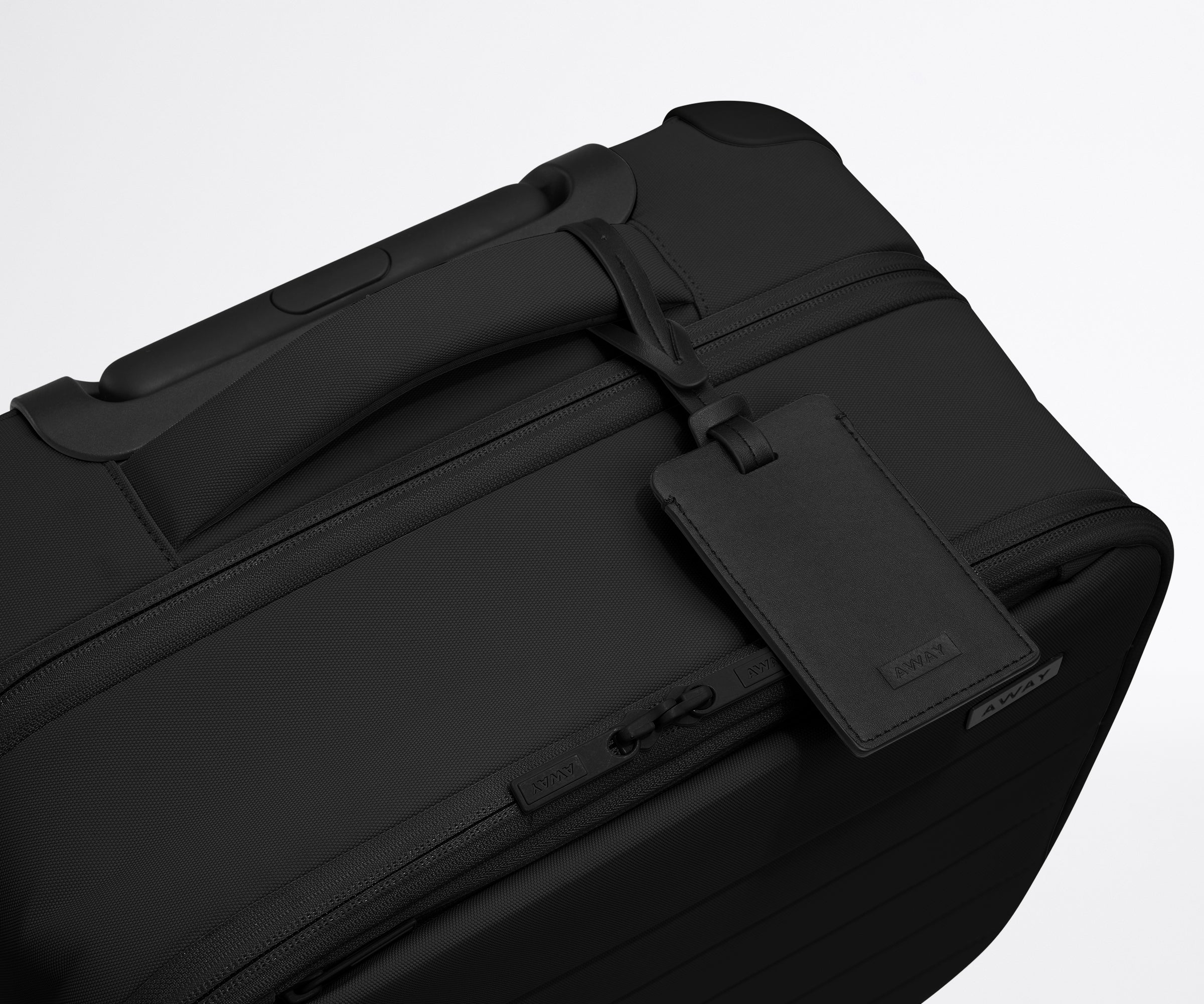 The Softside Compact Carry-On suitcase in Jet Black shown shown from above highlighting the recycled leather luggage tag