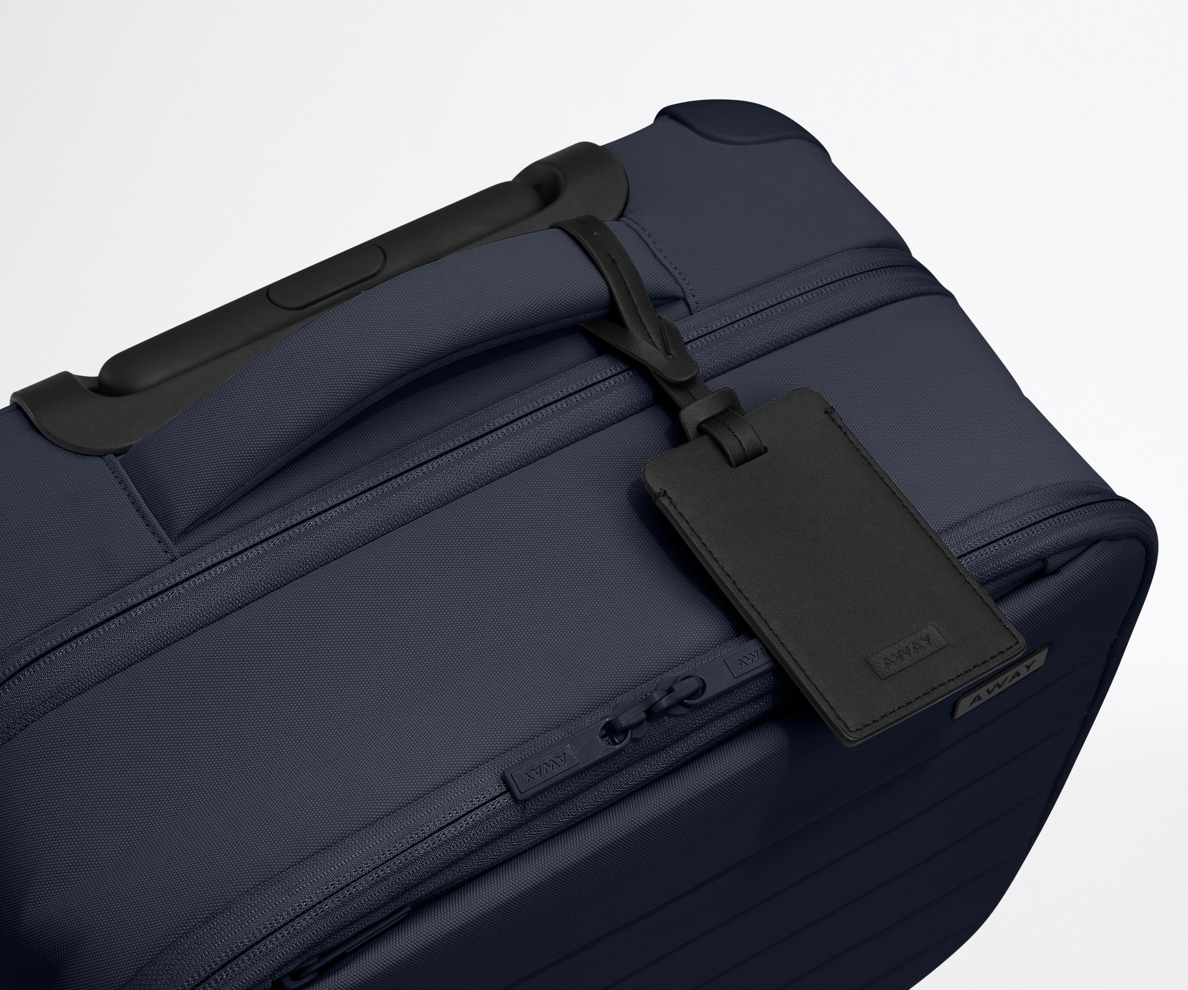The Softside Compact Carry-On suitcase in Navy Blue shown shown from above highlighting the recycled leather luggage tag