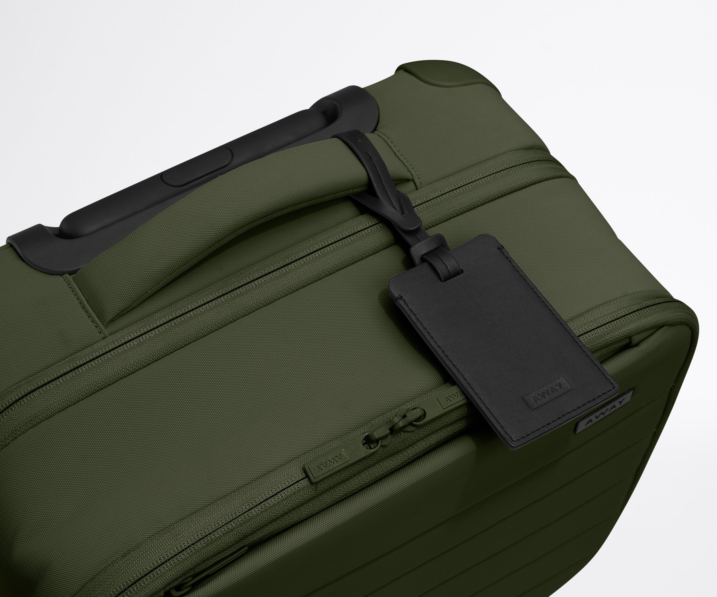 The Softside Compact Carry-On suitcase in Olive Green shown shown from above highlighting the recycled leather luggage tag