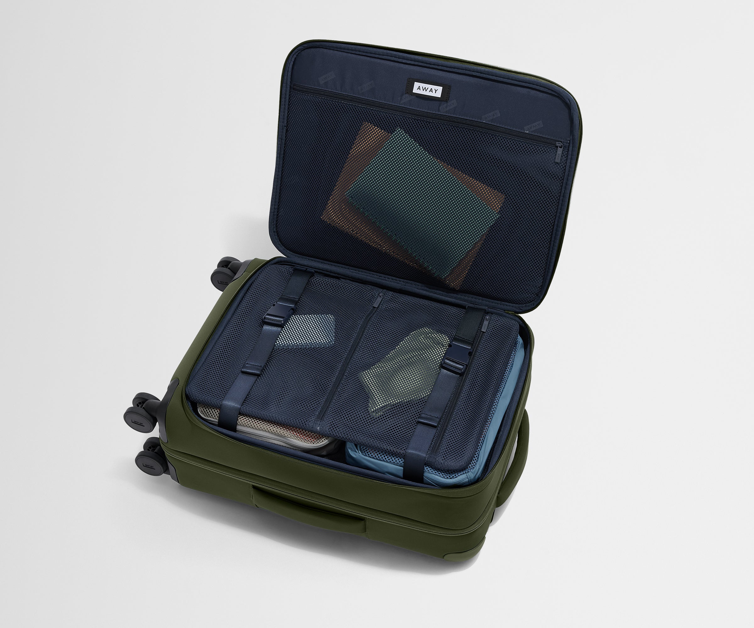 The Softside Bigger Carry-On suitcase in Olive Green shown open on its side and packed with Away's packing organizers to show capacity and the interior compression system, designed to help you pack more in