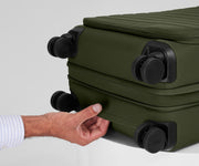 The Softside Carry-On suitcase in Olive Green shown laying on a surface to highlight the underside grab handle