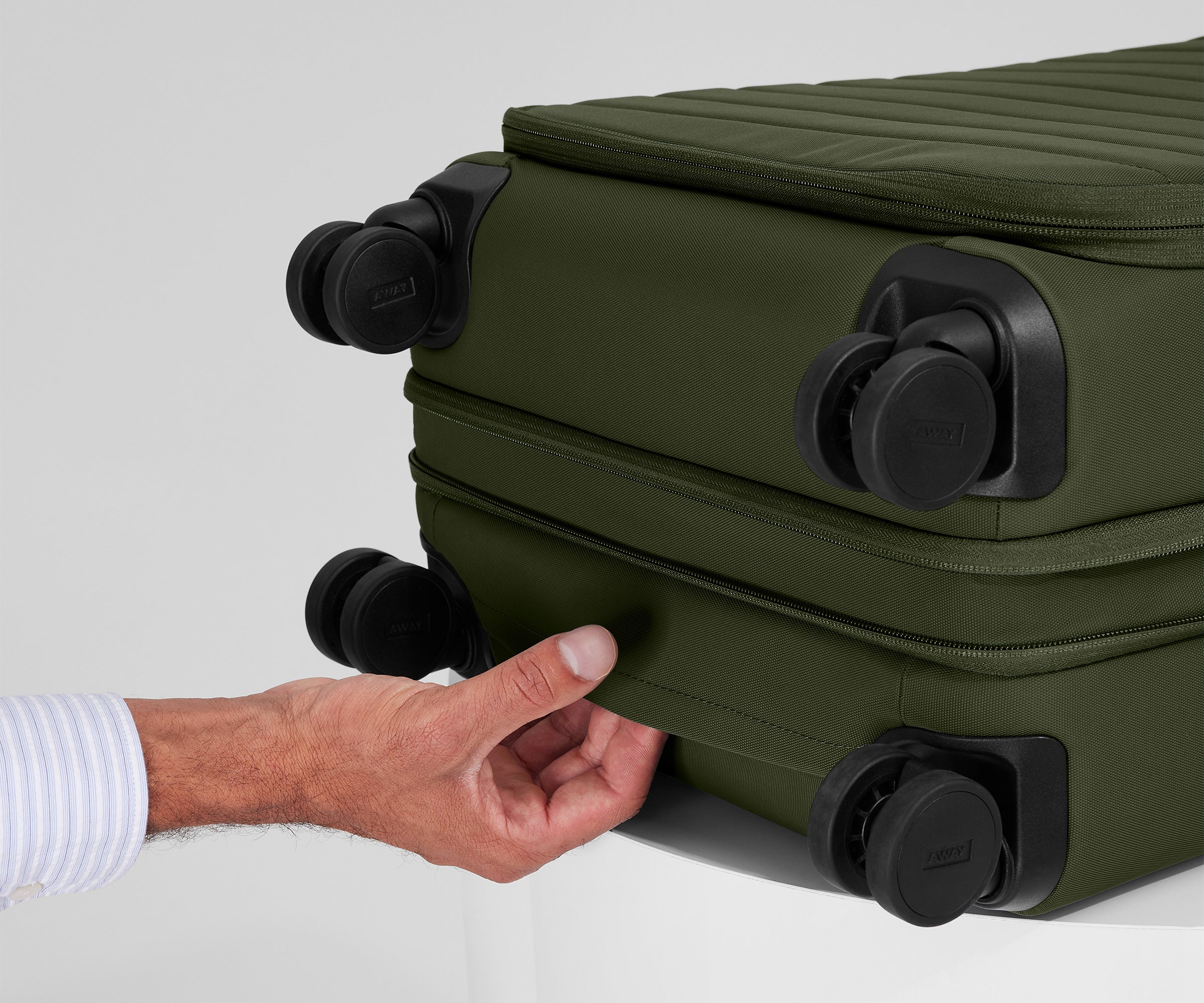 The Softside Carry-On suitcase in Olive Green shown laying on a surface to highlight the underside grab handle