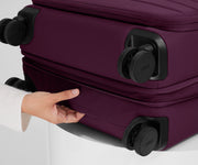 The Softside Medium suitcase in Plum Purple shown laying on a surface to highlight the underside grab handle