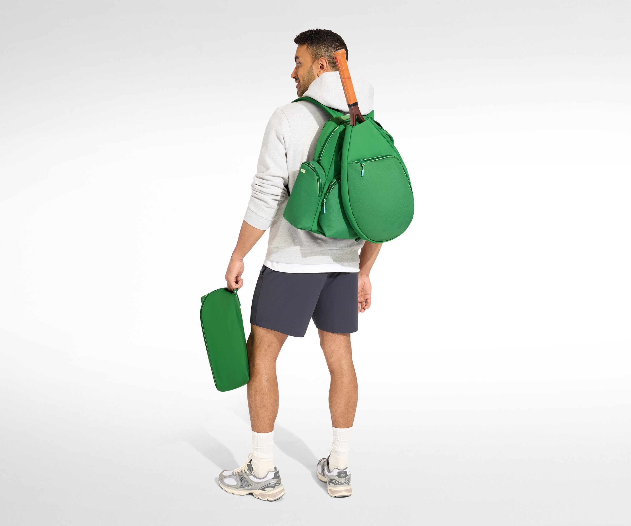 Man holding a green backpack and green shoe bag on a white background
