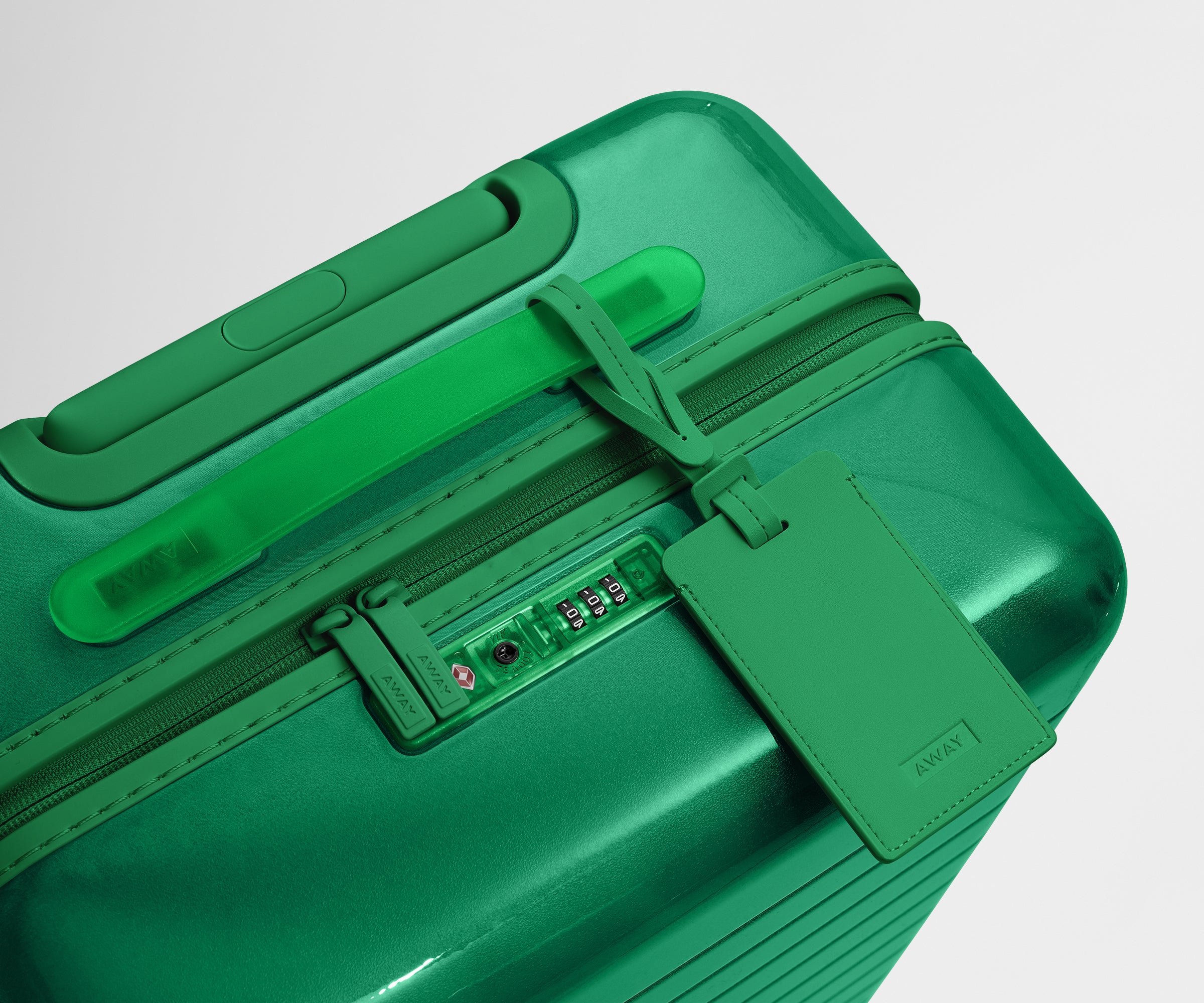 The Bigger Carry-On suitcase in Translucent Green shown shown from above highlighting TSA-approved combination lock and recycled, color-matched leather luggage tag