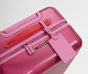 The Bigger Carry-On suitcase in Translucent Pink shown shown from above highlighting TSA-approved combination lock and recycled, color-matched leather luggage tag