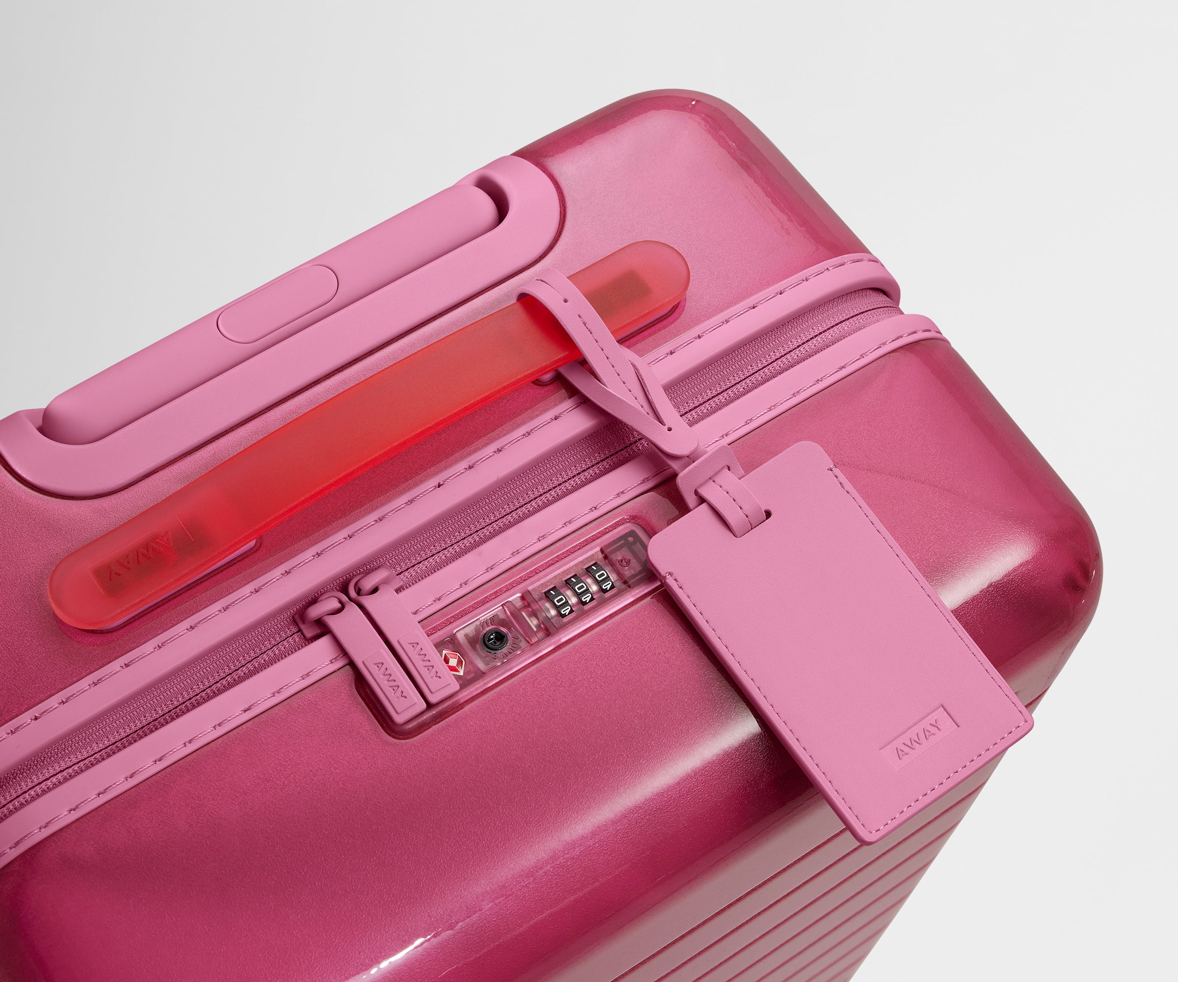 The Bigger Carry-On suitcase in Translucent Pink shown shown from above highlighting TSA-approved combination lock and recycled, color-matched leather luggage tag