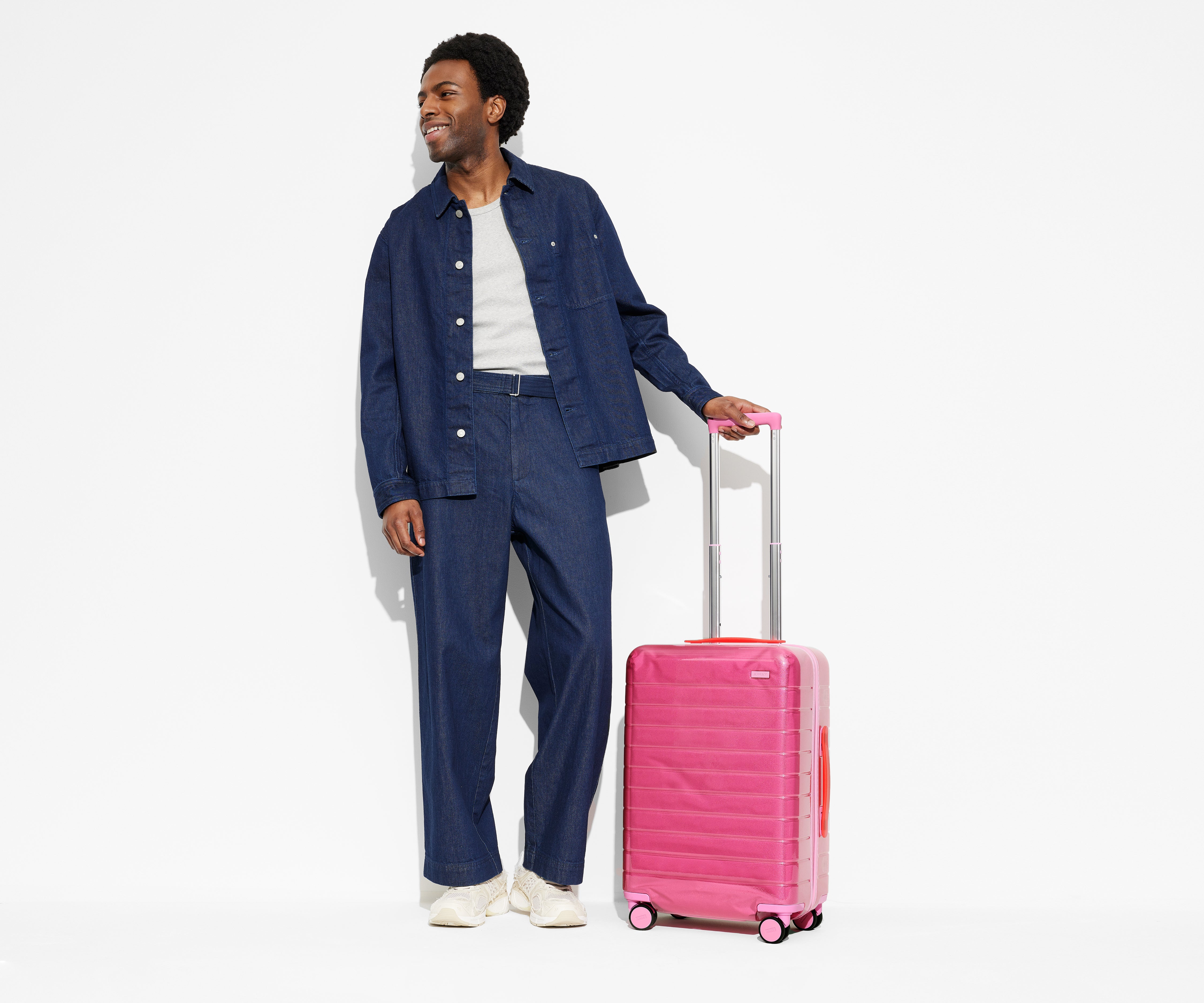 A 6'2" model standing next to The Bigger Carry-On suitcase in Translucent Pink with the raised handle to show size and scale