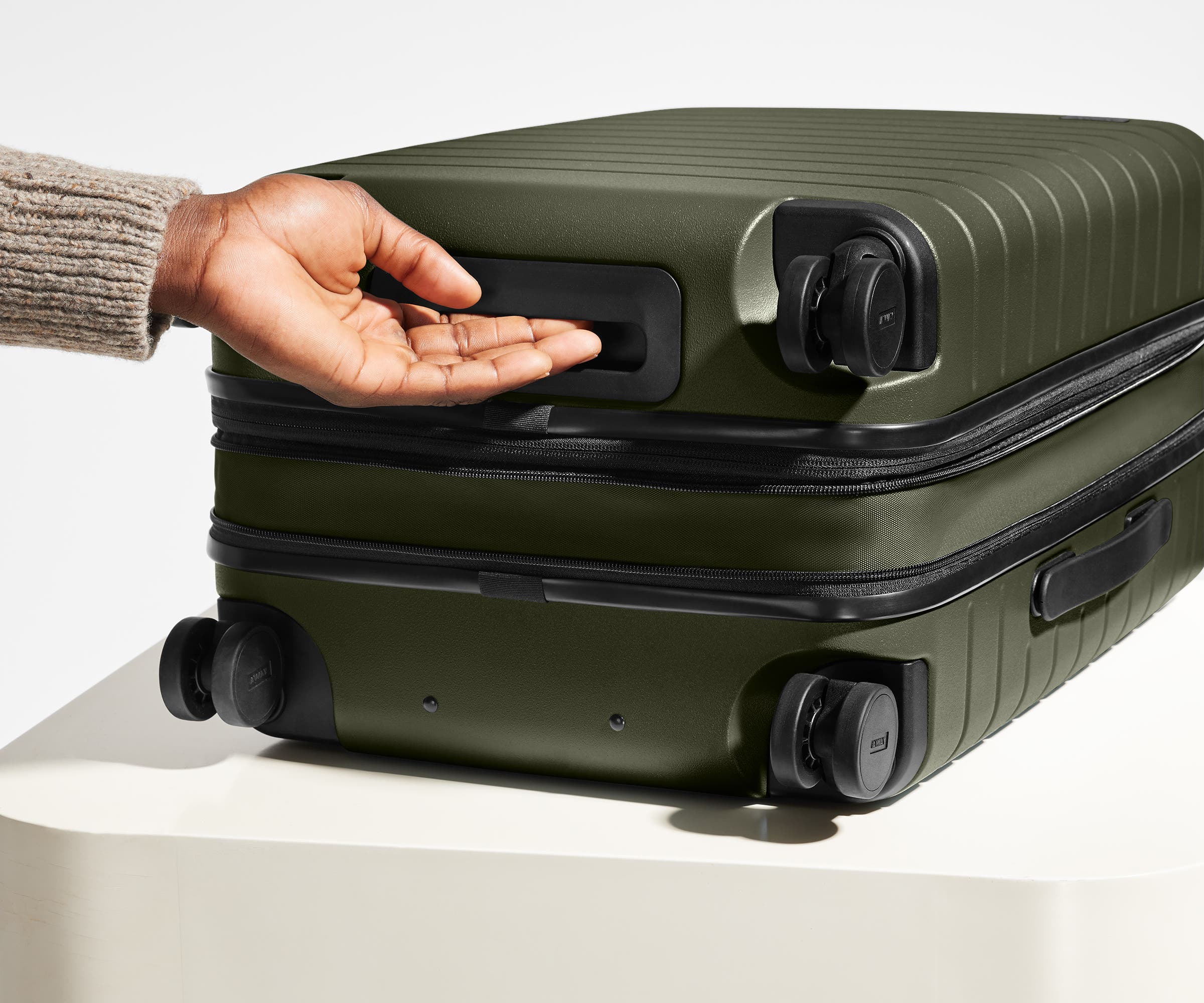 The Bigger Carry-On Flex suitcase in Olive Green shown from below highlighting the underside grab handle