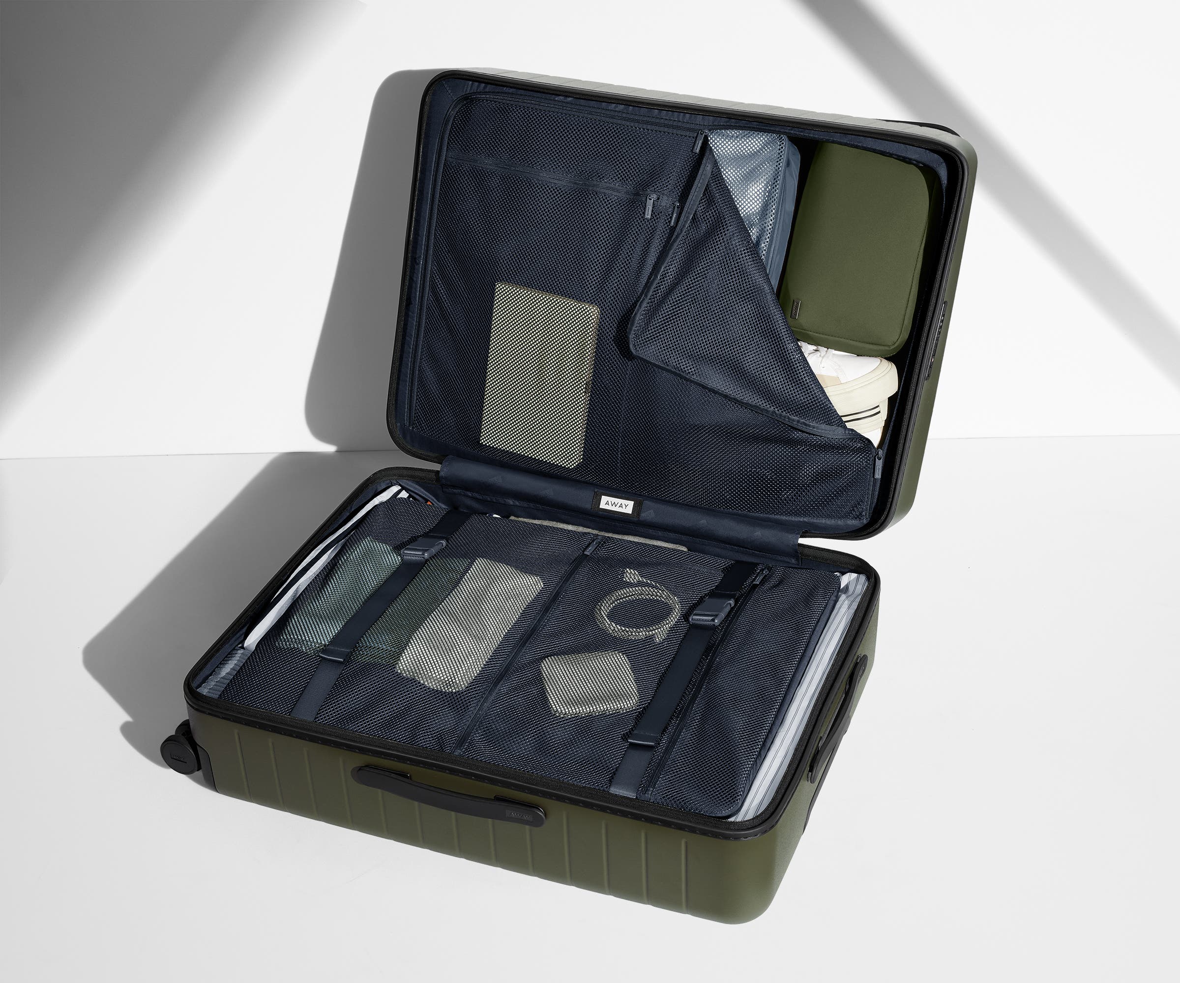The Large suitcase in Olive Green shown open on its side and packed with Away's packing organizers to show capacity and the interior compression system, designed to help you pack more in