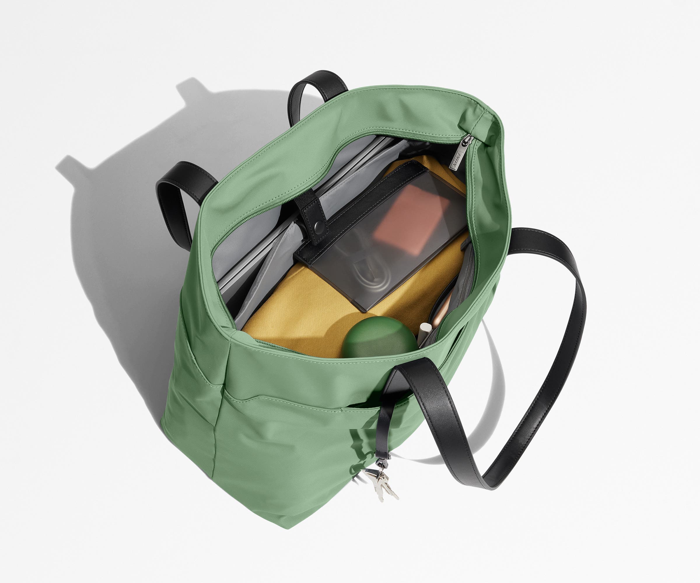 Tote bag packed with a laptop, water bottle, travel pouch, and sweater. A key is attached to the hidden key leash