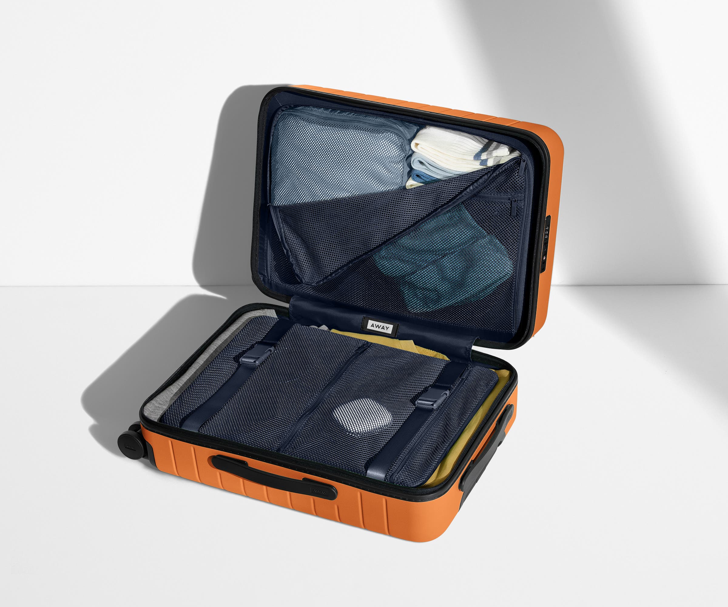 The Carry-On suitcase in Sorbet Orange shown open on its side and packed with Away's packing organizers to show capacity and the interior compression system, designed to help you pack more in
