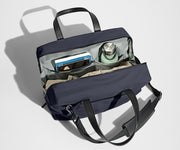 Main compartment packed with a light sweater, notebook, tablet, and water bottle. The detachable shoulder strap is clipped onto the bag.