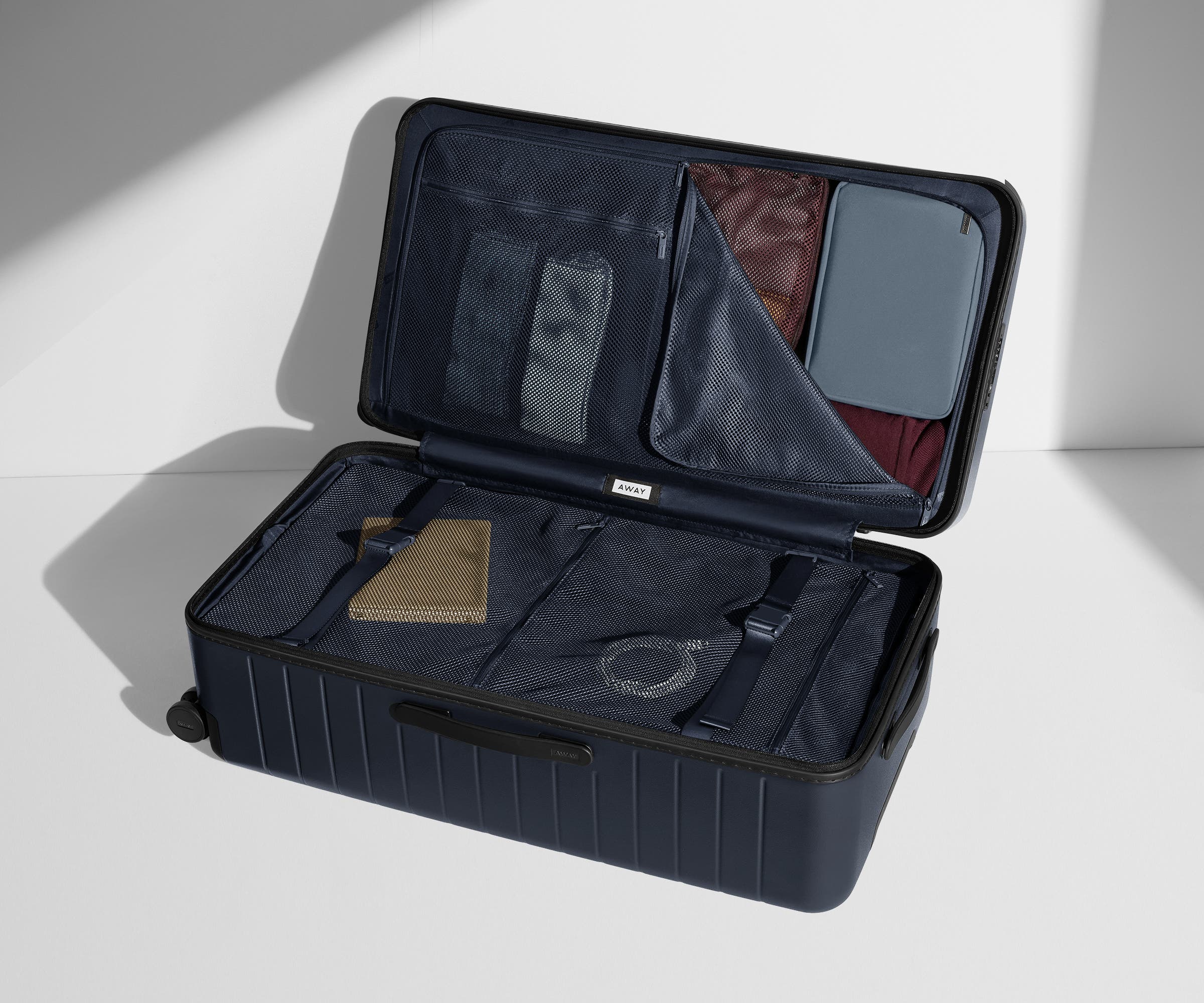 The Trunk suitcase in Navy Blue shown open on its side and packed with Away's packing organizers to show capacity and the interior compression system, designed to help you pack more in