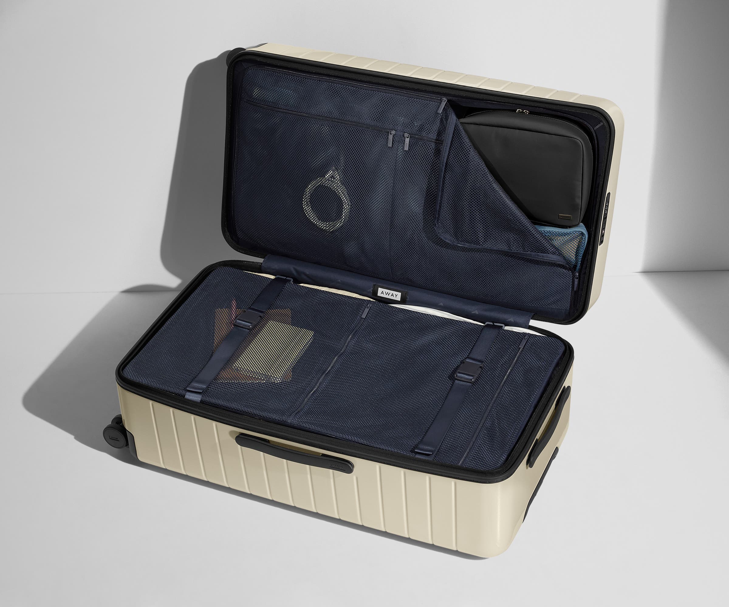 The Trunk suitcase in Salt White (Gloss) shown open on its side and packed with Away's packing organizers to show capacity and the interior compression system, designed to help you pack more in