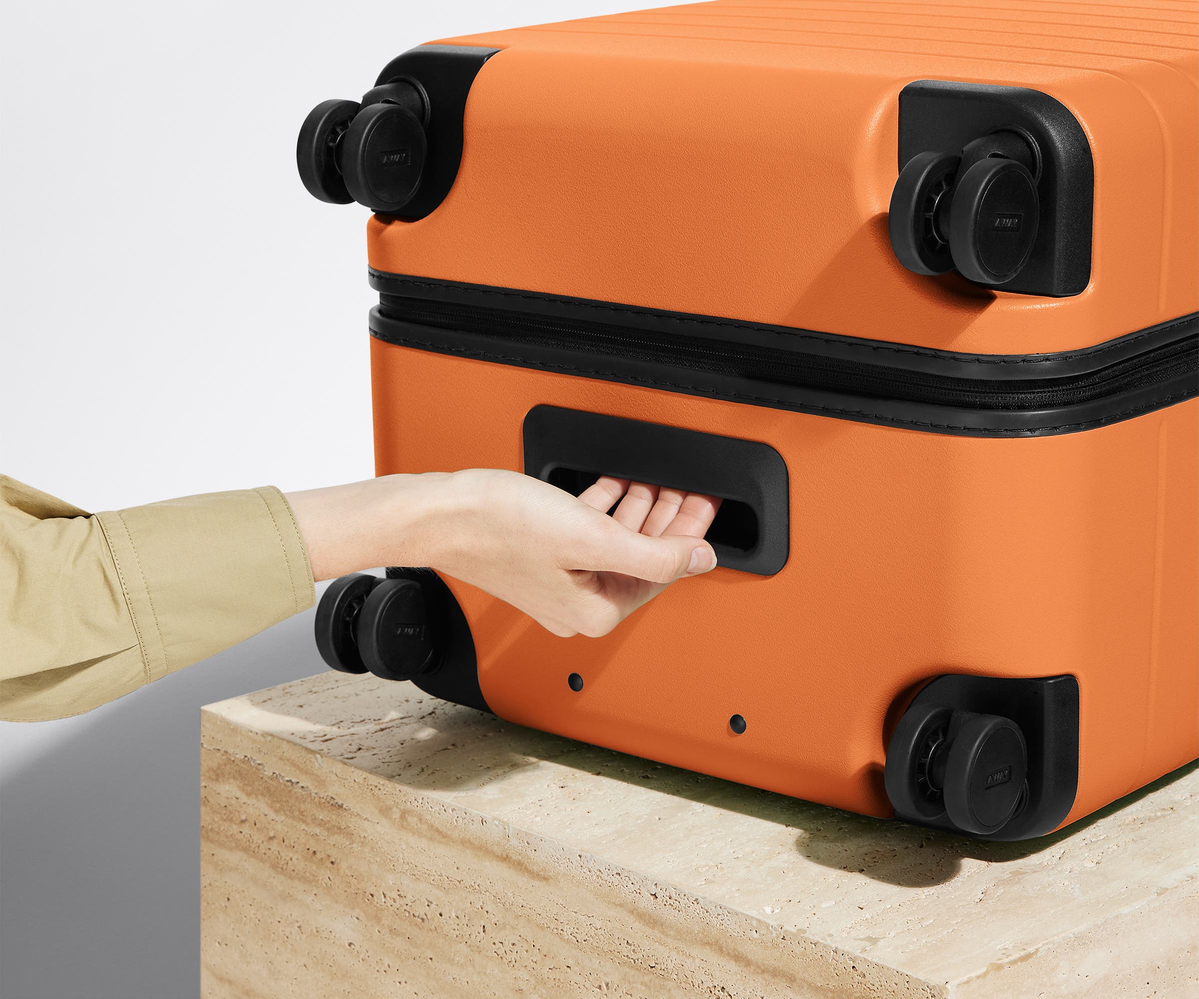 The Trunk suitcase in Sorbet Orange shown from below highlighting the underside grab handle