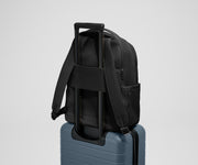 The Commuter Backpack on top of an Away suitcase, attached by the trolley pass-through sleeve