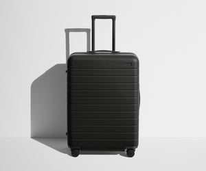 Front product view of The Medium suitcase in Jet Black with raised handle