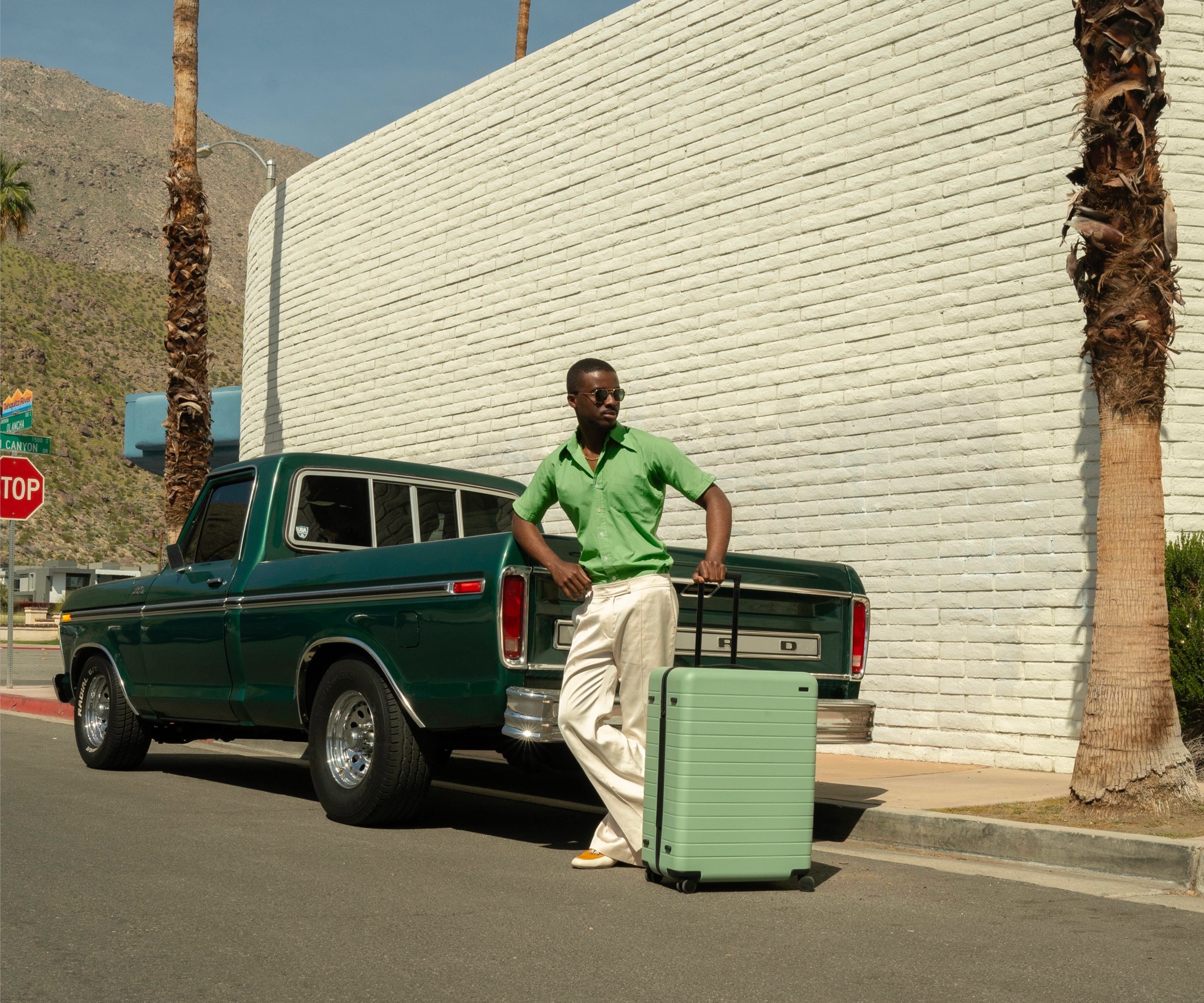 Influencer @danclemt posing against a retro green truck and California street backdrop with The Large suitcase in Sea Green