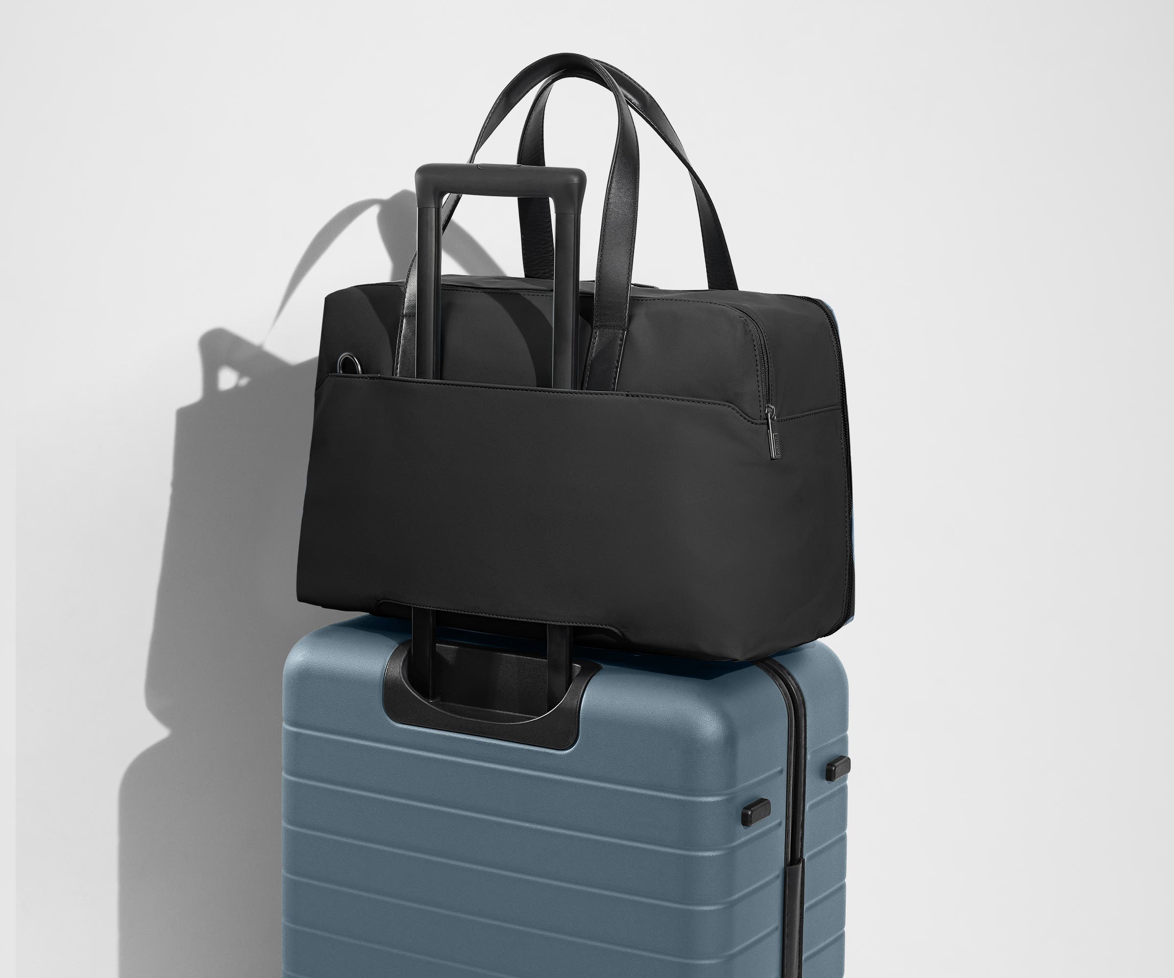 The Overnight Bag secured to an Away checked suitcase using the trolley sleeve