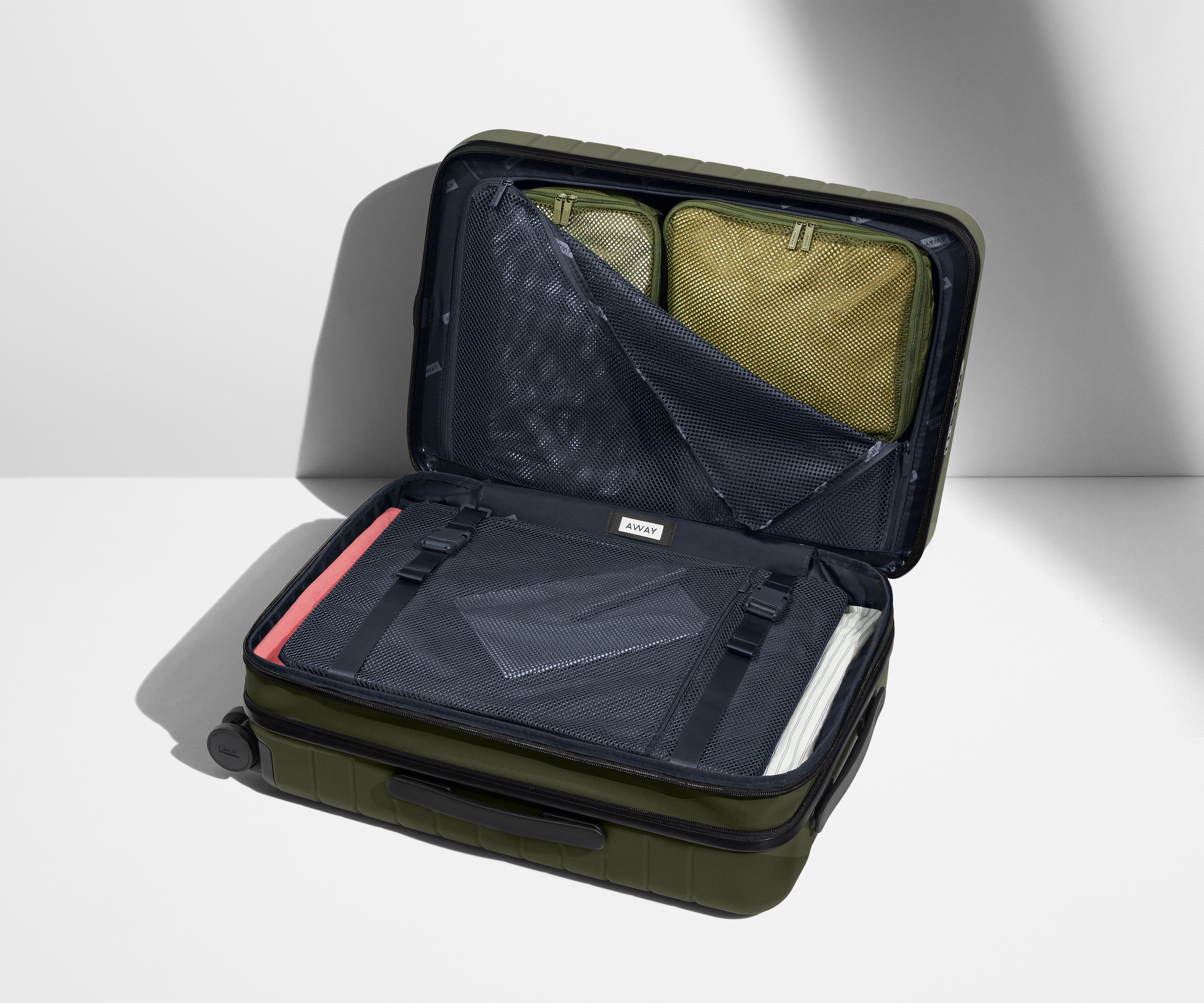 The Carry-On Flex suitcase in Olive Green shown open on its side and packed with Away's packing organizers to show capacity and the interior compression system, designed to help you pack more in