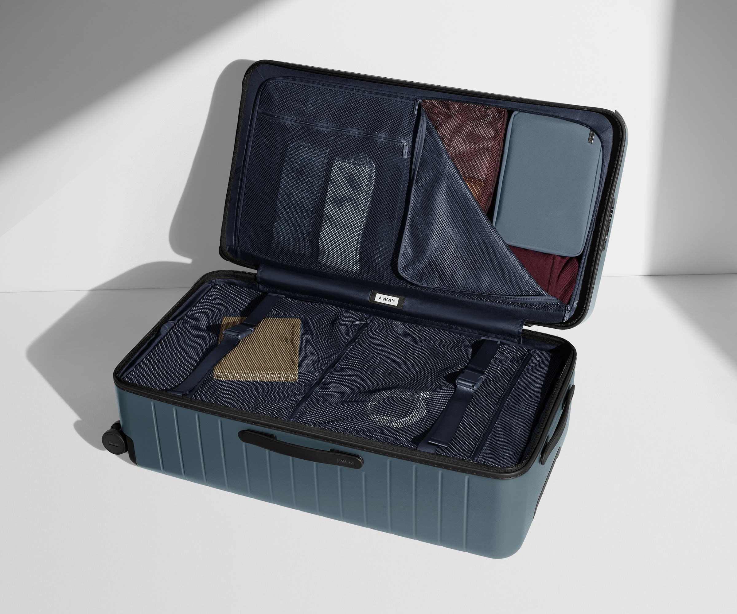 The Trunk suitcase in Coast Blue shown open on its side and packed with Away's packing organizers to show capacity and the interior compression system, designed to help you pack more in