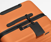 The Trunk suitcase in Sorbet Orange shown shown from above highlighting TSA-approved combination lock and recycled leather luggage tag