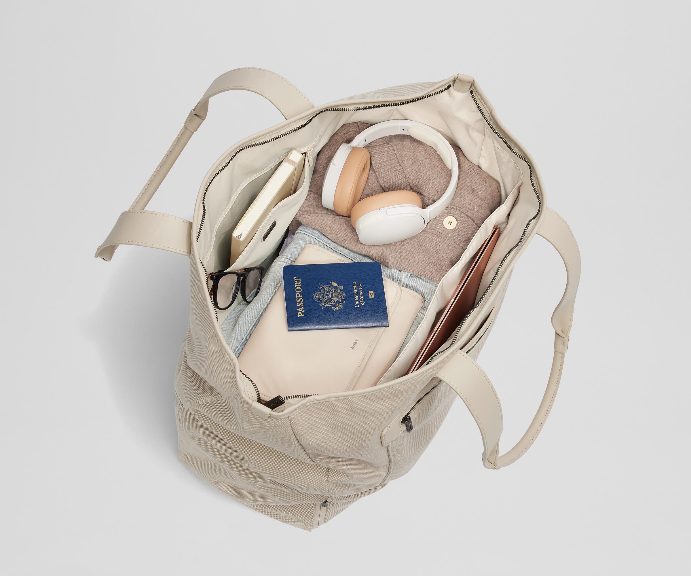 Top-down view of the tote packed with clothing, passport, headphones, a notebook, and a laptop among other travel essentials
