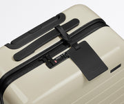 The Bigger Carry-On suitcase in Salt White (Gloss) shown shown from above highlighting TSA-approved combination lock and recycled leather luggage tag