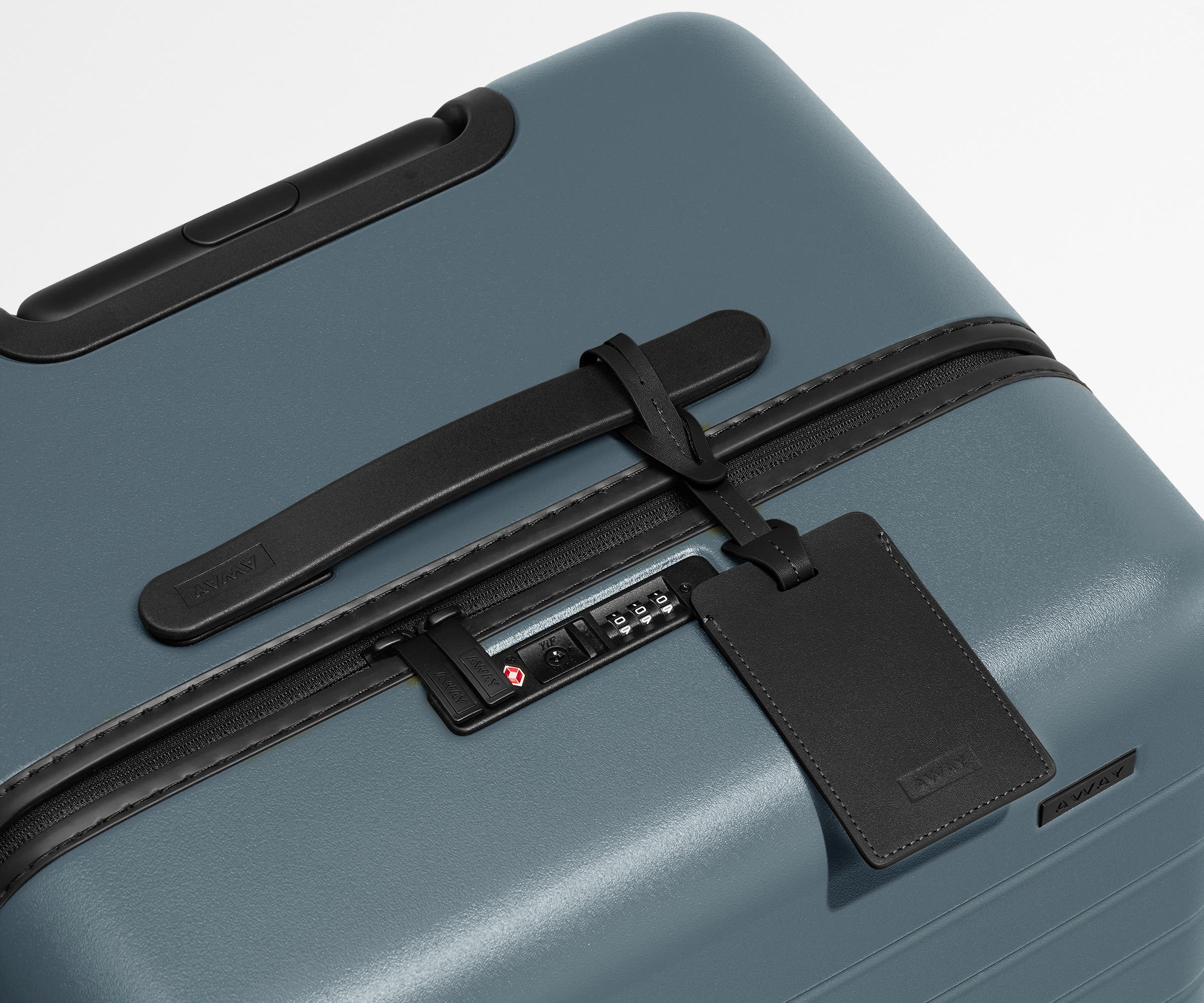 The Trunk suitcase in Coast Blue shown shown from above highlighting TSA-approved combination lock and recycled leather luggage tag